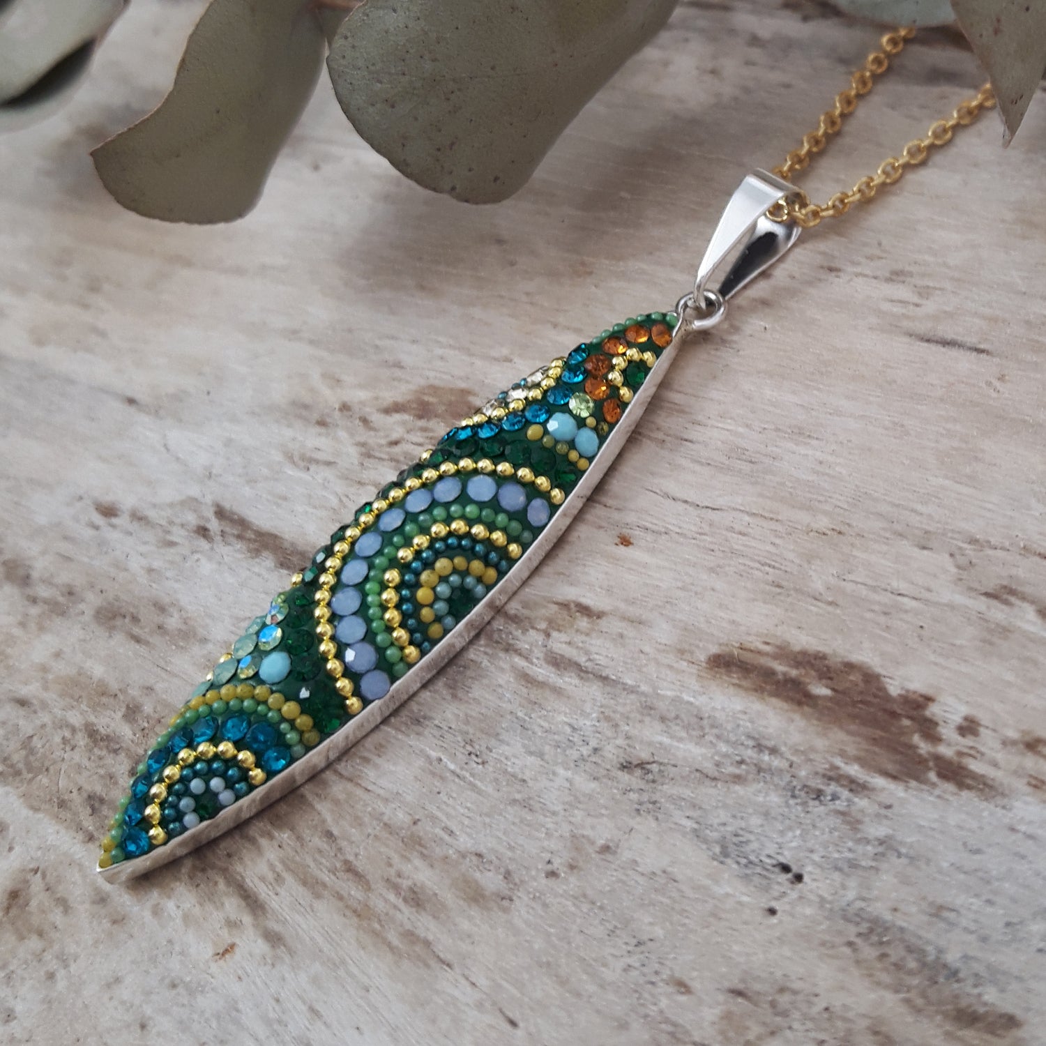 Decorative micro-pearl and crystal pendant with colourful beads on a gold chain, placed on a wooden surface.