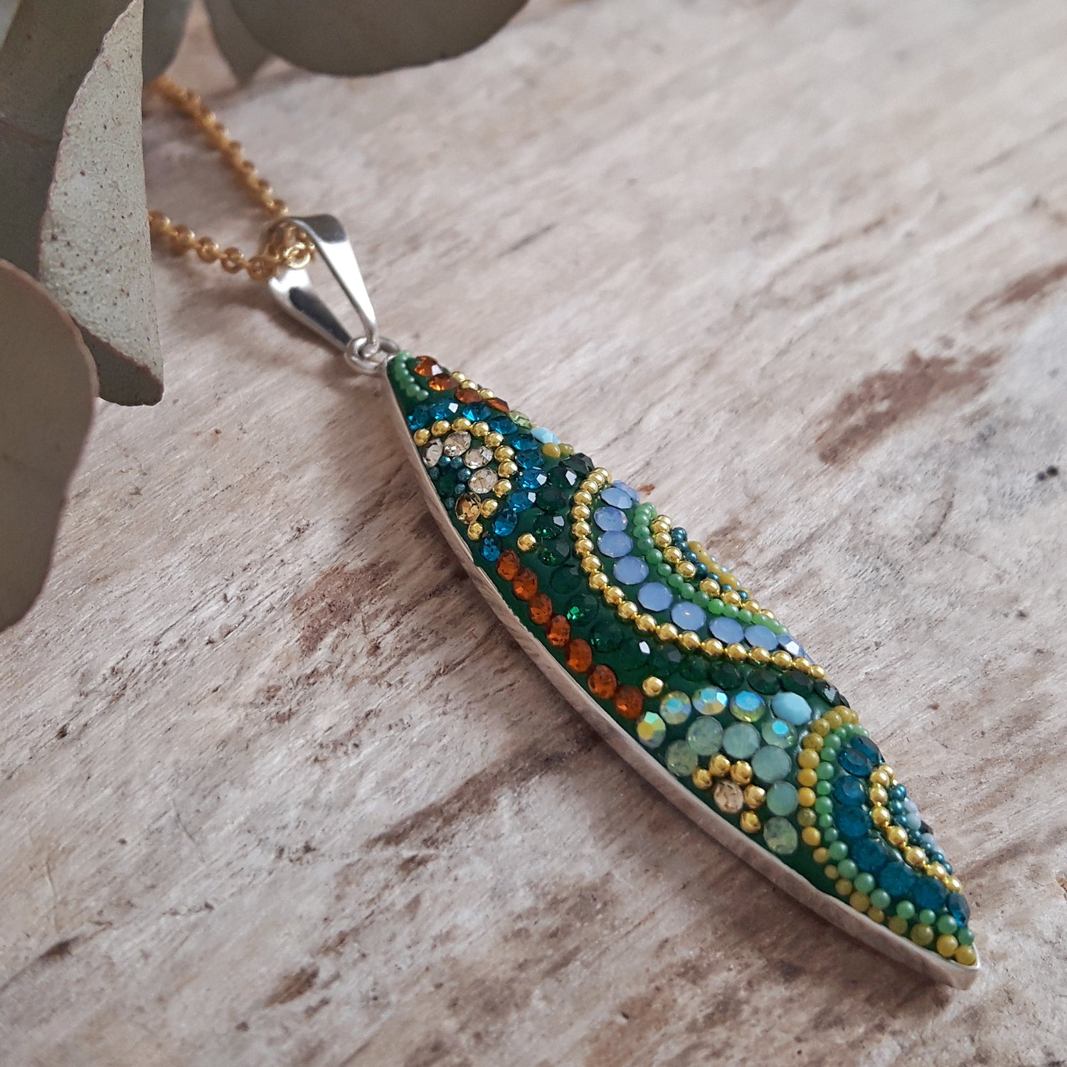 Decorative micro-pearl and crystal pendant on a gold plated chain necklace on a wooden surface
