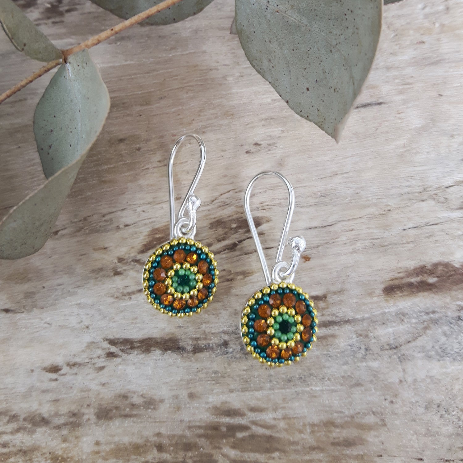 Pair of micro-bead and crystal drop earrings on a wooden surface with leaves in the background