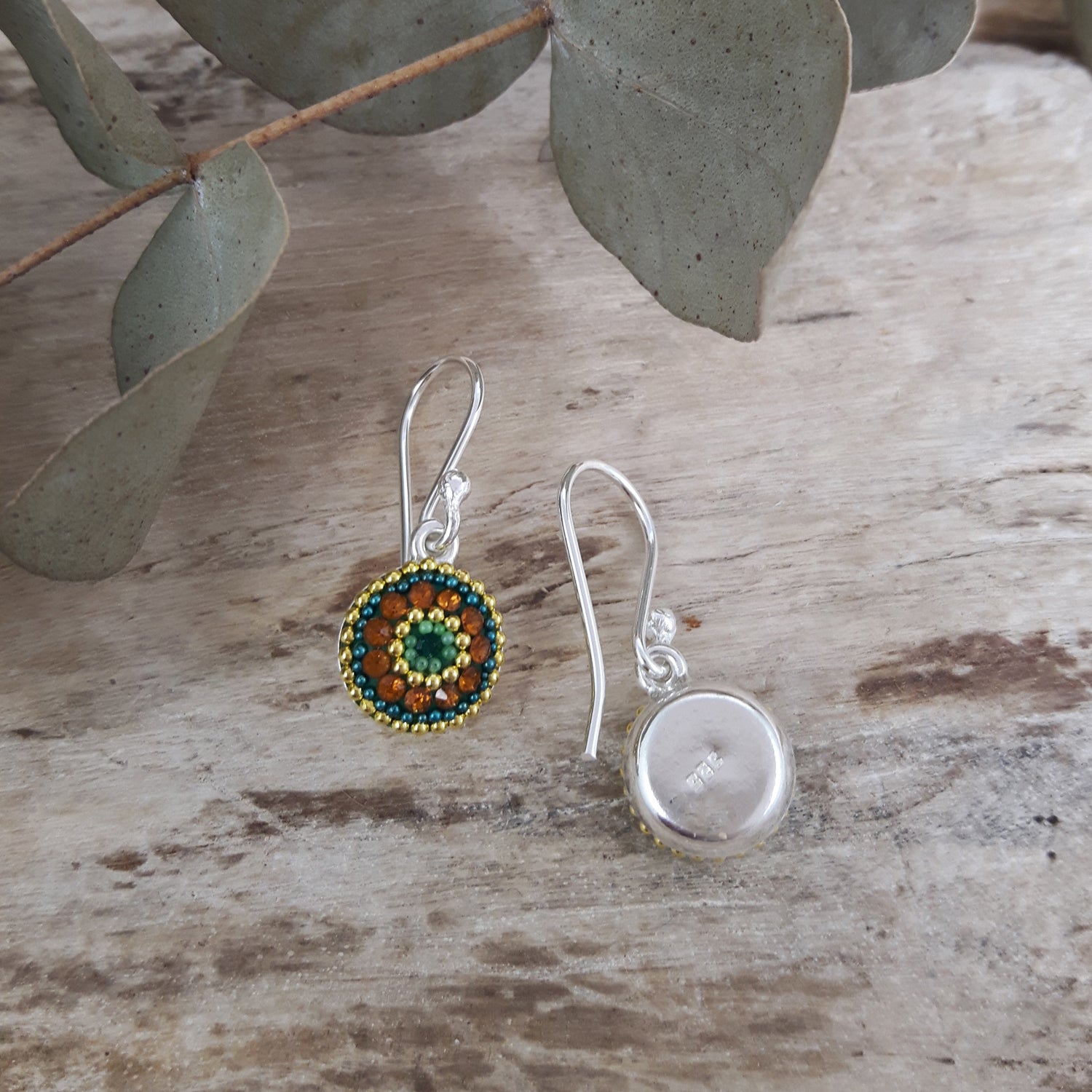 Two earrings on a wooden surface with leaves in the background