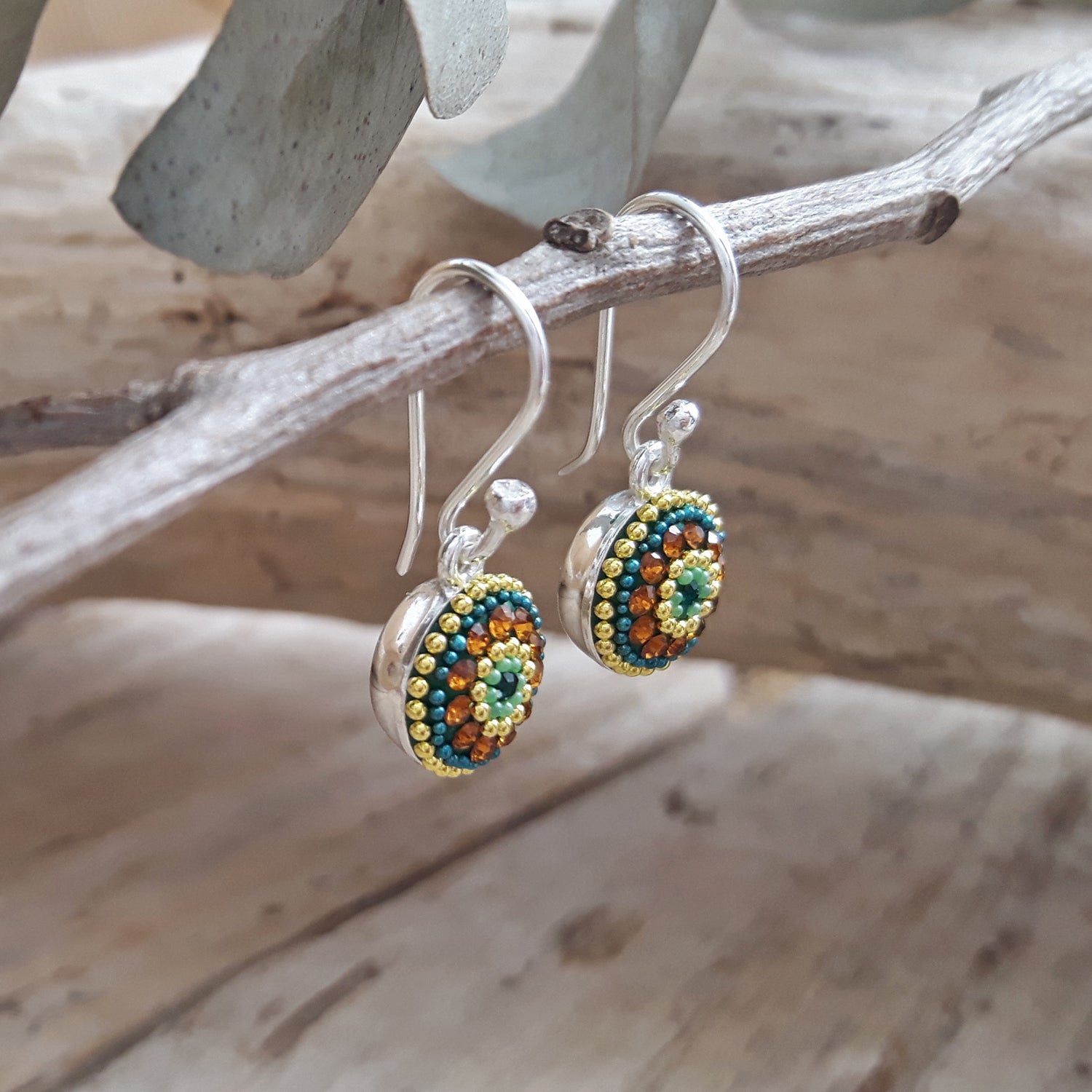 Colorful gold, green and amber micro-bead and crystal drop earrings on a branch with a natural background