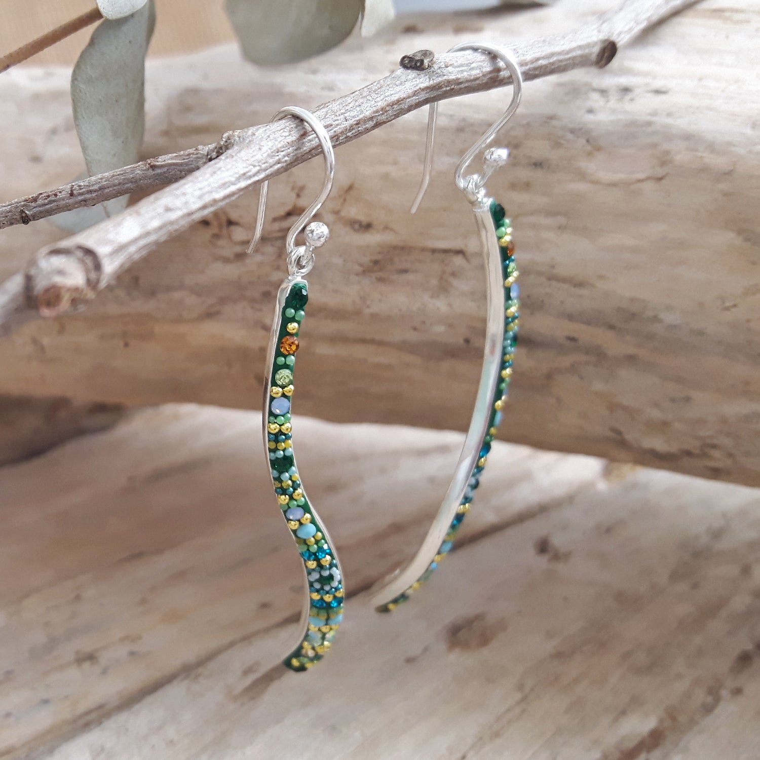 Wavy beaded earrings hanging from a branch on a wooden surface