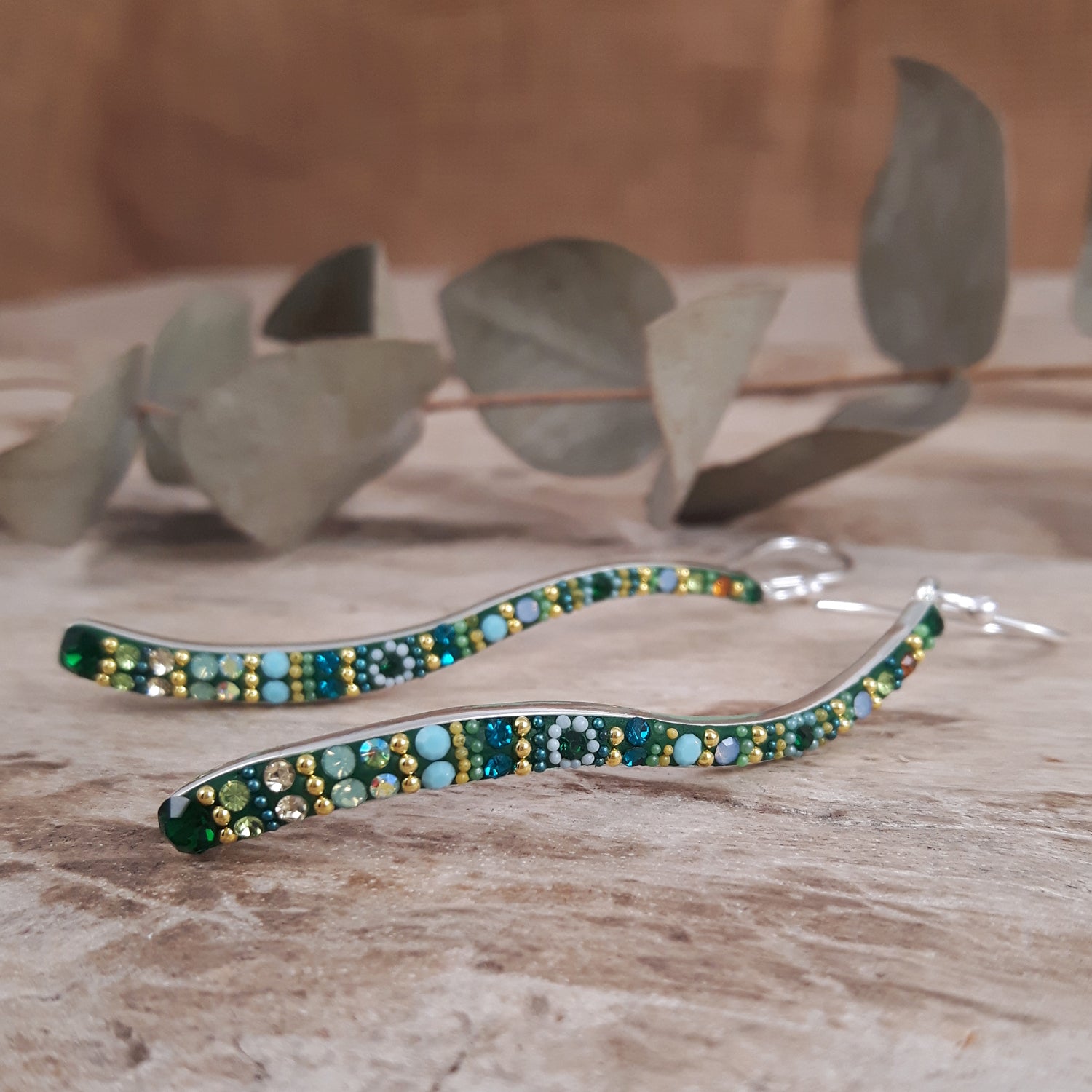 Micro-bead and crystal sterling silver earrings on a wooden surface with eucalyptus leaves in the background