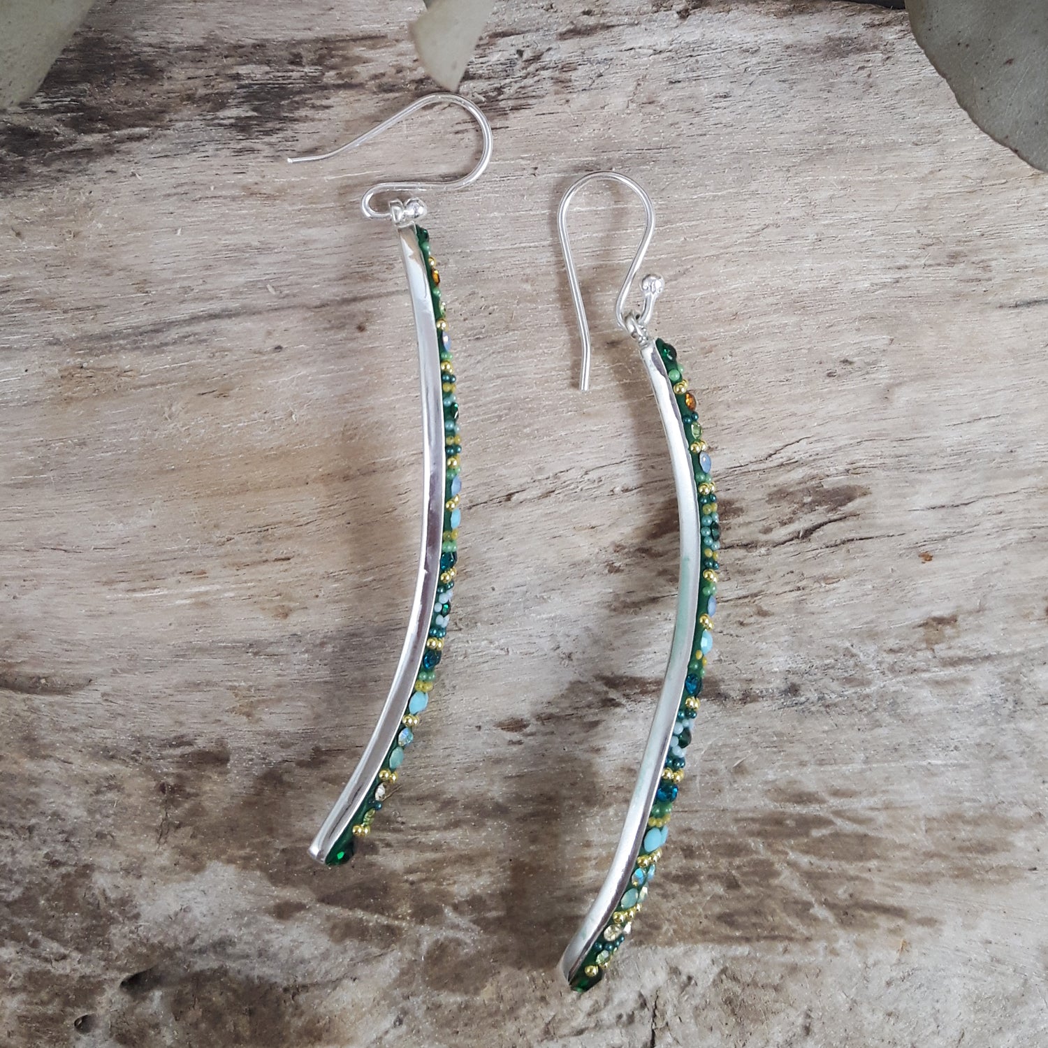 Sterling silver earrings with hand-applied green and blue micro-beads and crystals on a wooden surface