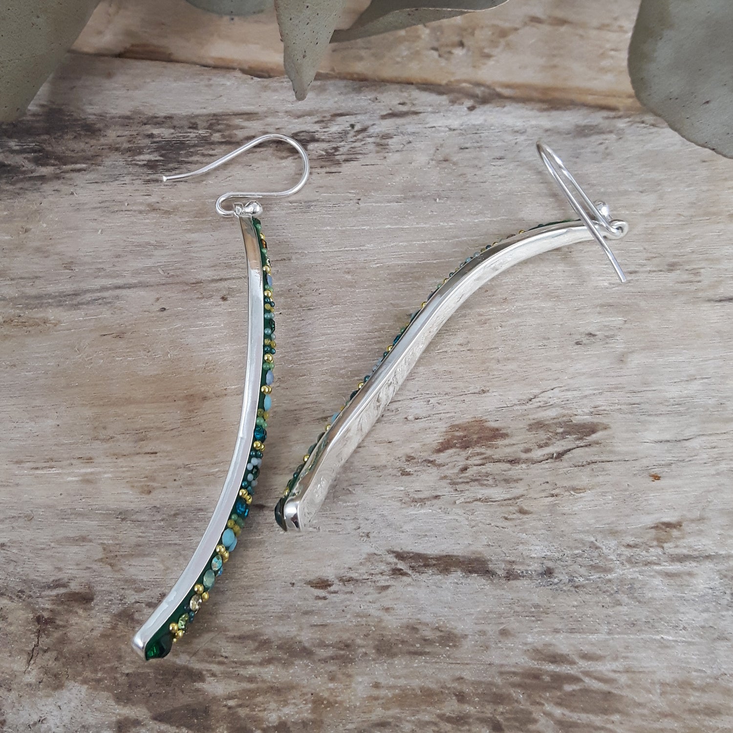 Sterling silver earrings with green and gold beads on a wooden surface