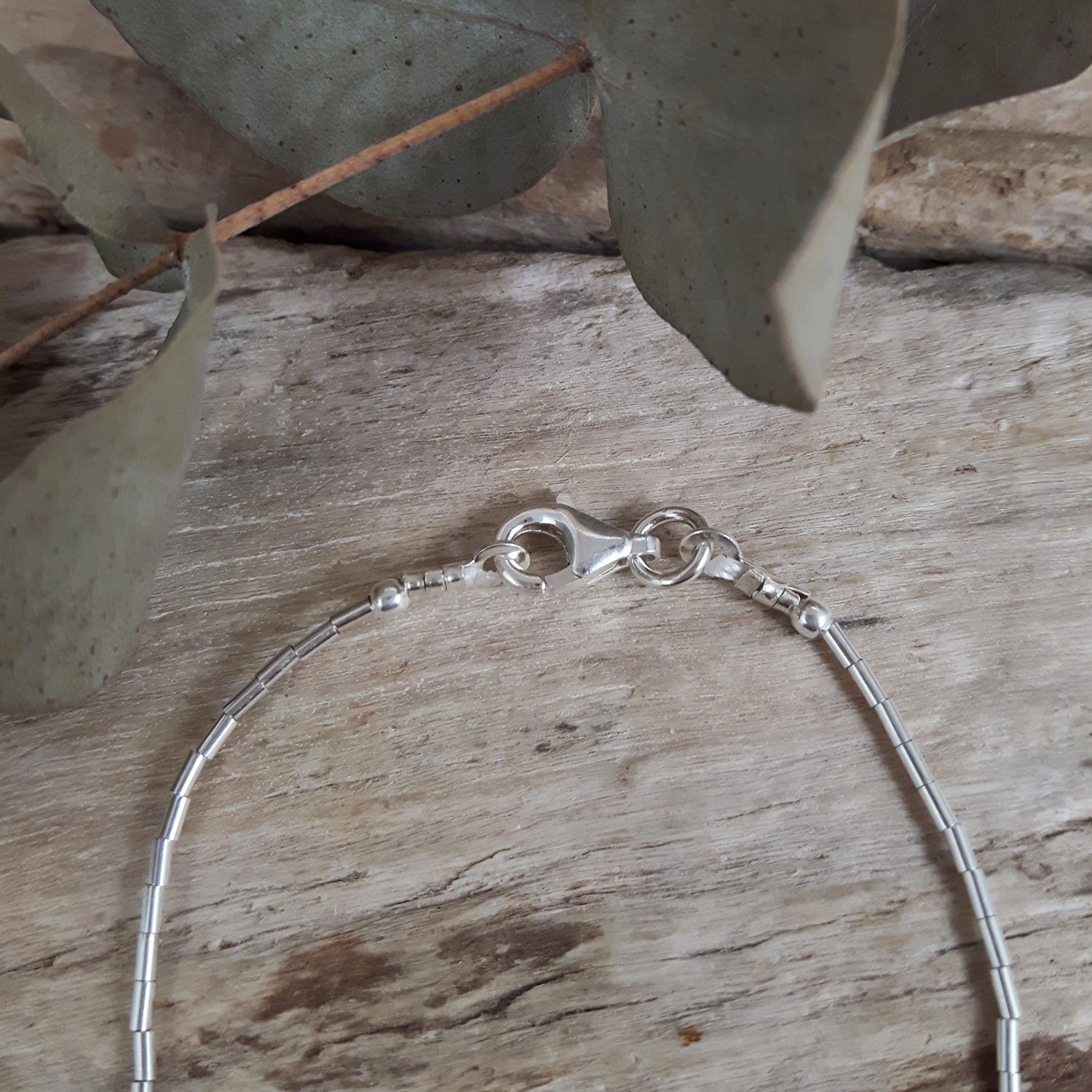 Sterling silver bracelet on a wooden surface with leaves in the background