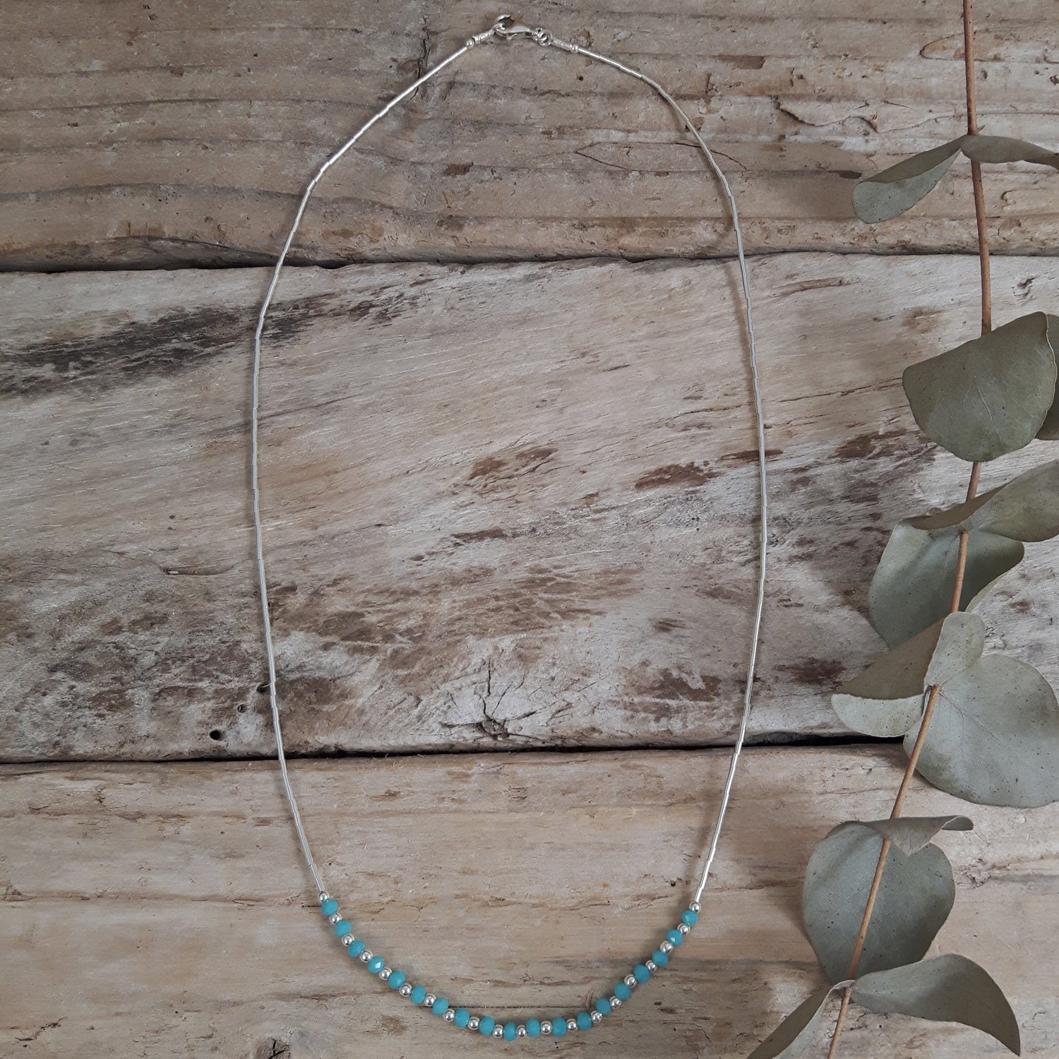 Necklace with blue chalcedony beads on a wooden surface with eucalyptus leaves