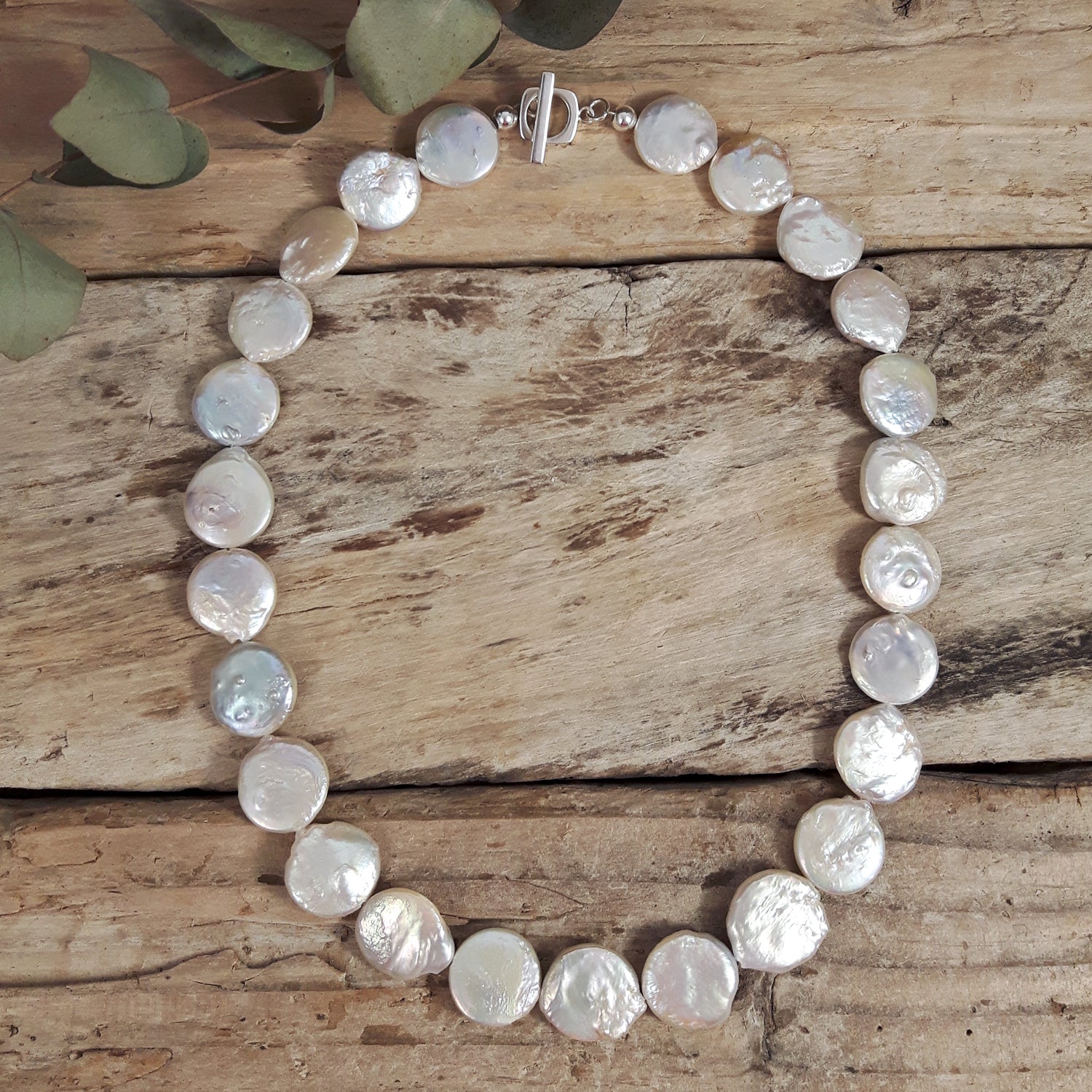 Baroque pearl necklace on a wooden surface with green leaves