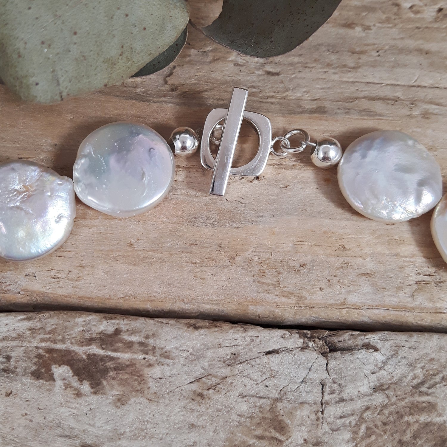 Silver T-bar detail with large round pearls on a wooden surface