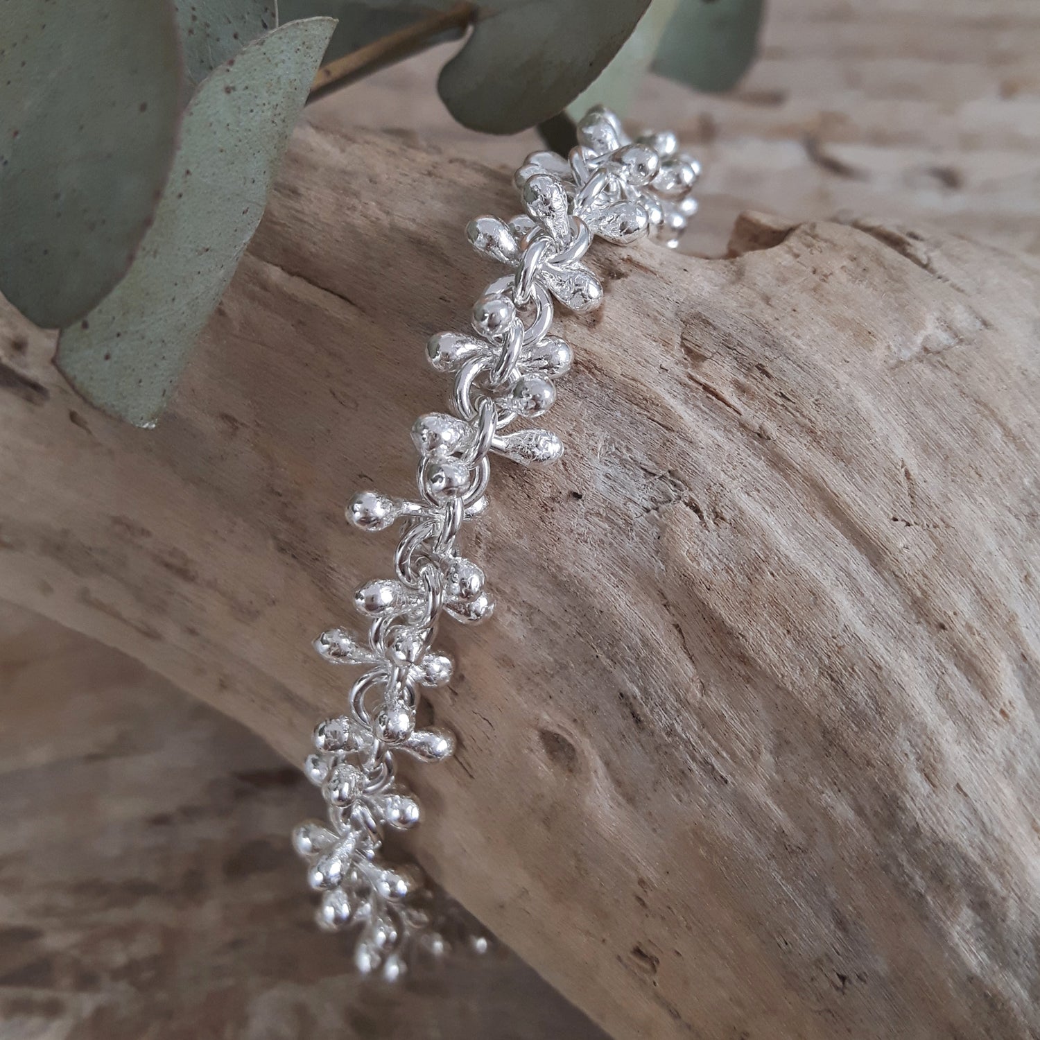 A sterling silver bracelet with a linked chain design, displayed on a wooden branch.