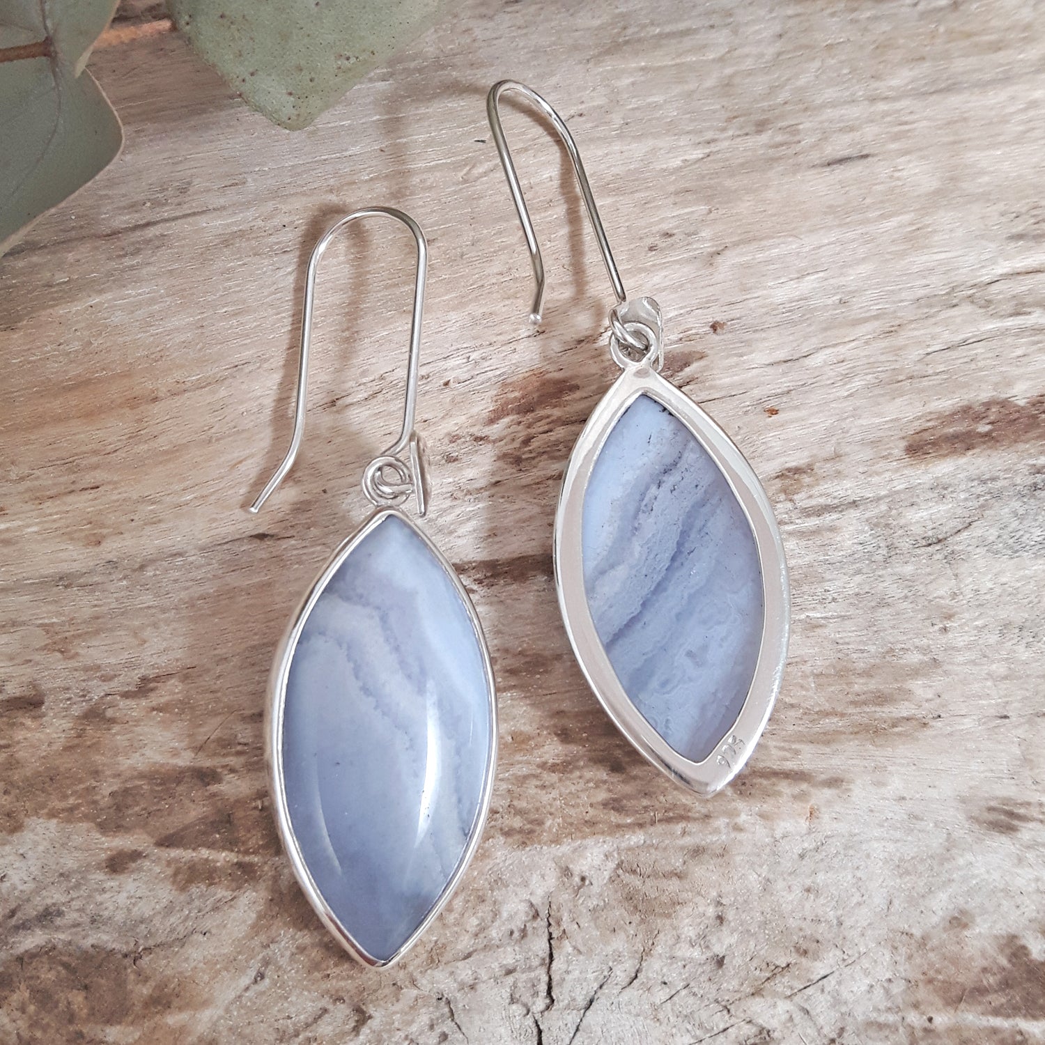 Silver earrings with blue stone drops on a wooden surface, showing front and back