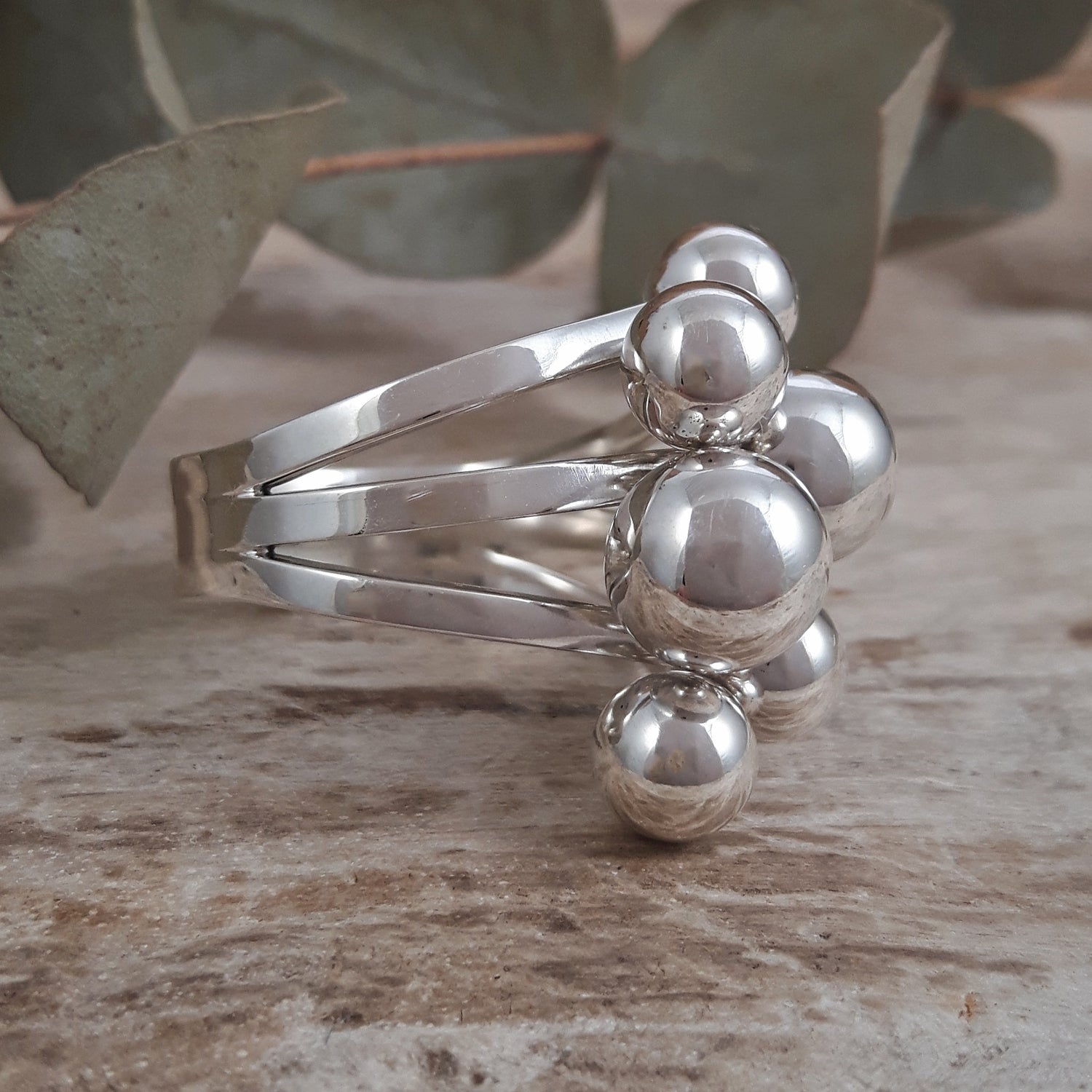 Polished sterling silver ring with spherical designs on a wooden surface with eucalyptus leaves in the background