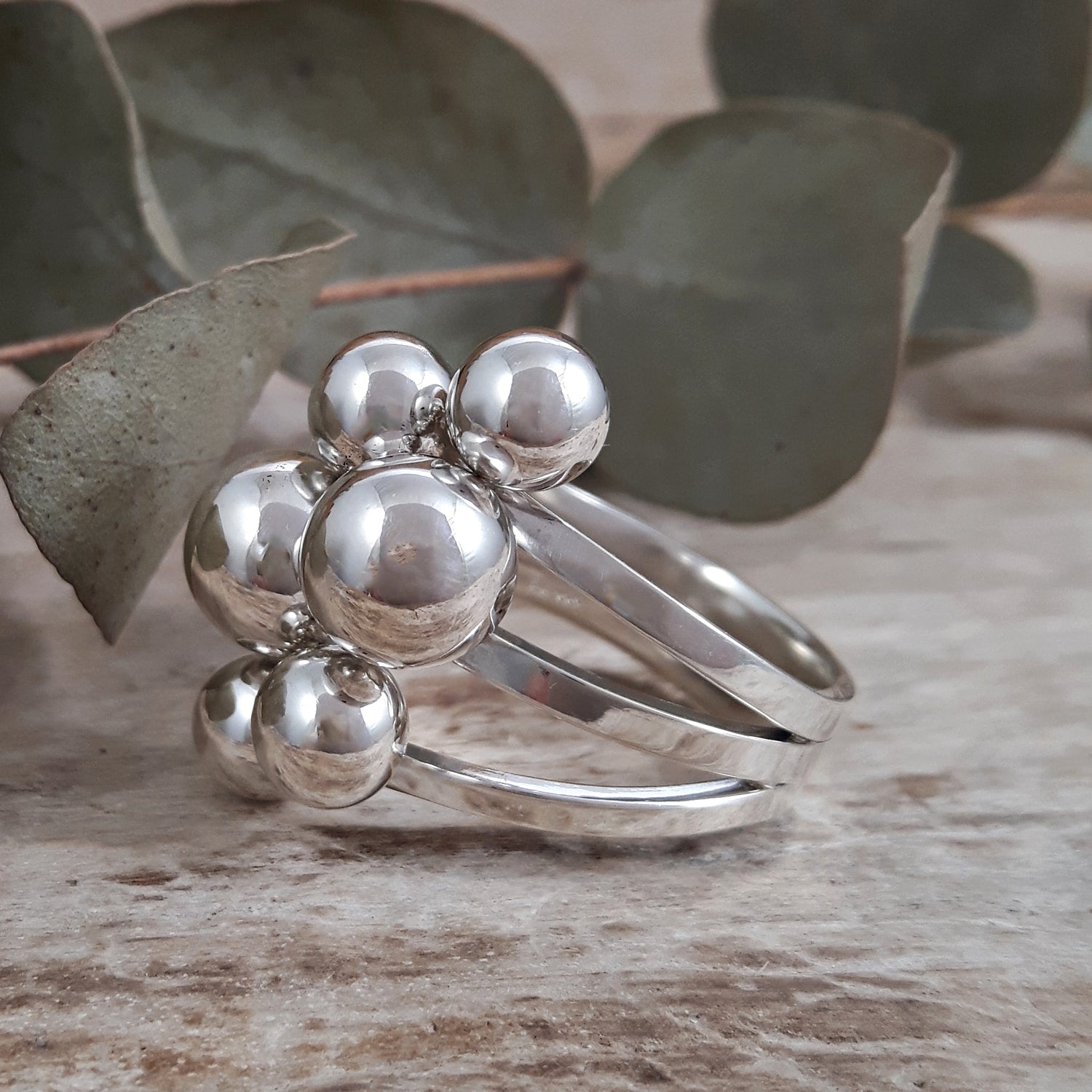 Sterling silver Calypso ring with spherical design on a wooden surface with eucalyptus leaves
