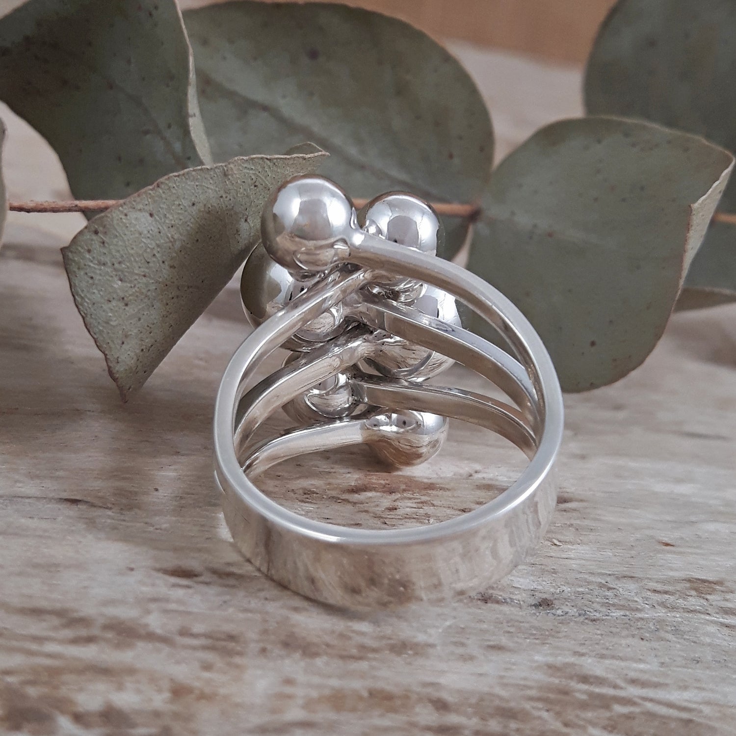 Polished sterling silver calypso ring with spherical elements on a wooden surface with leaves in the background