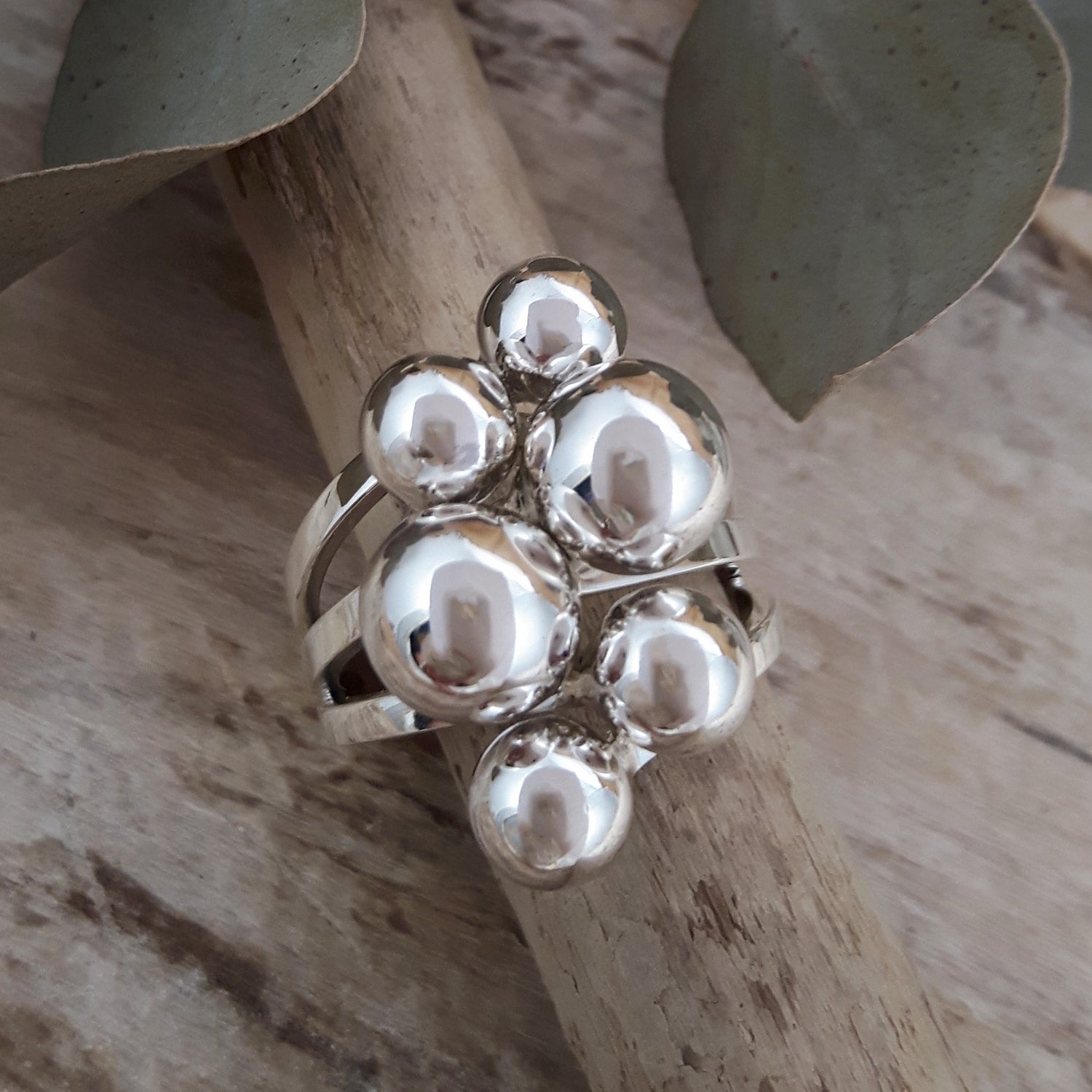 Polished sterling silver ring with spherical design on a wooden surface with leaves