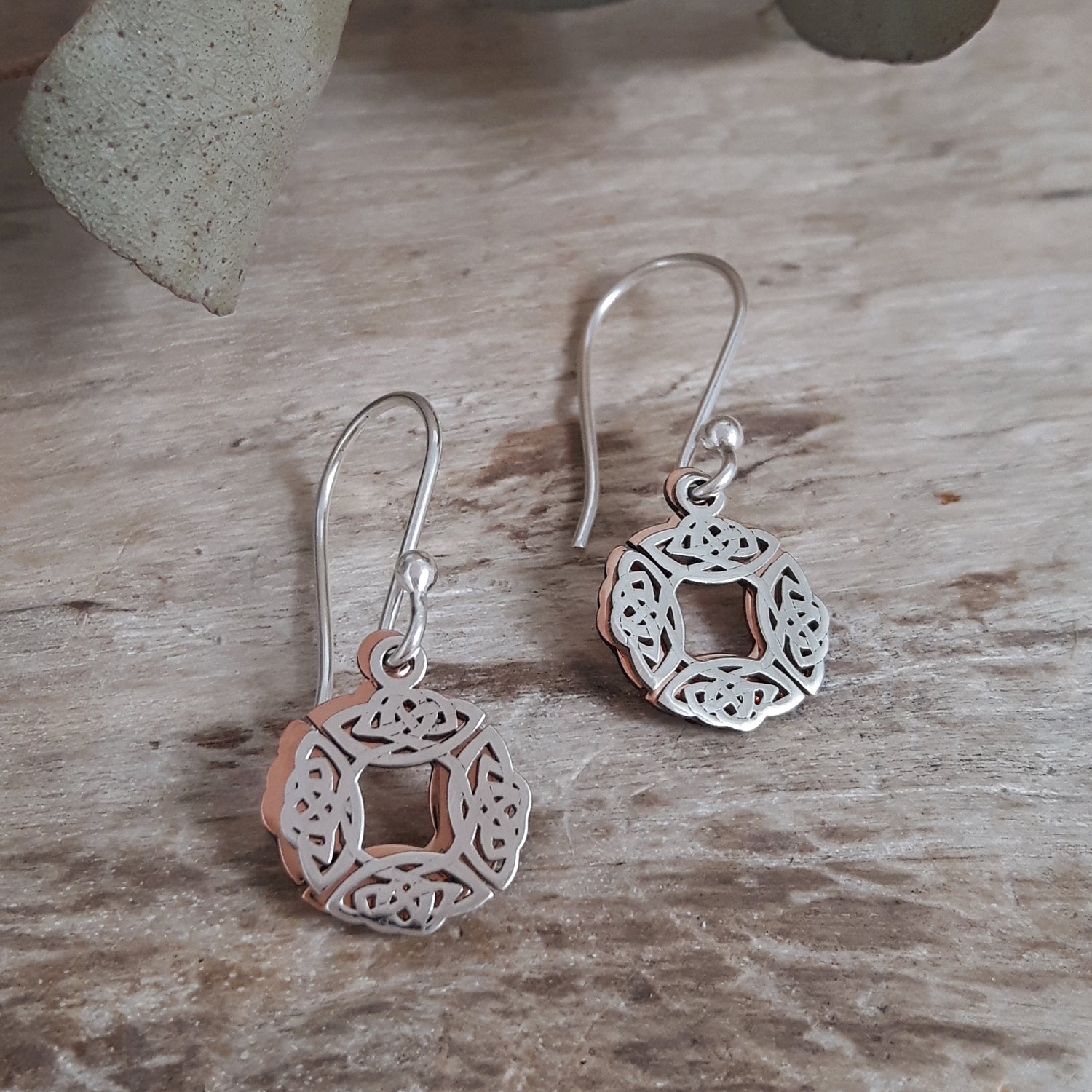 Sterling silver & copper Celtic Knot drop earrings on a wooden surface