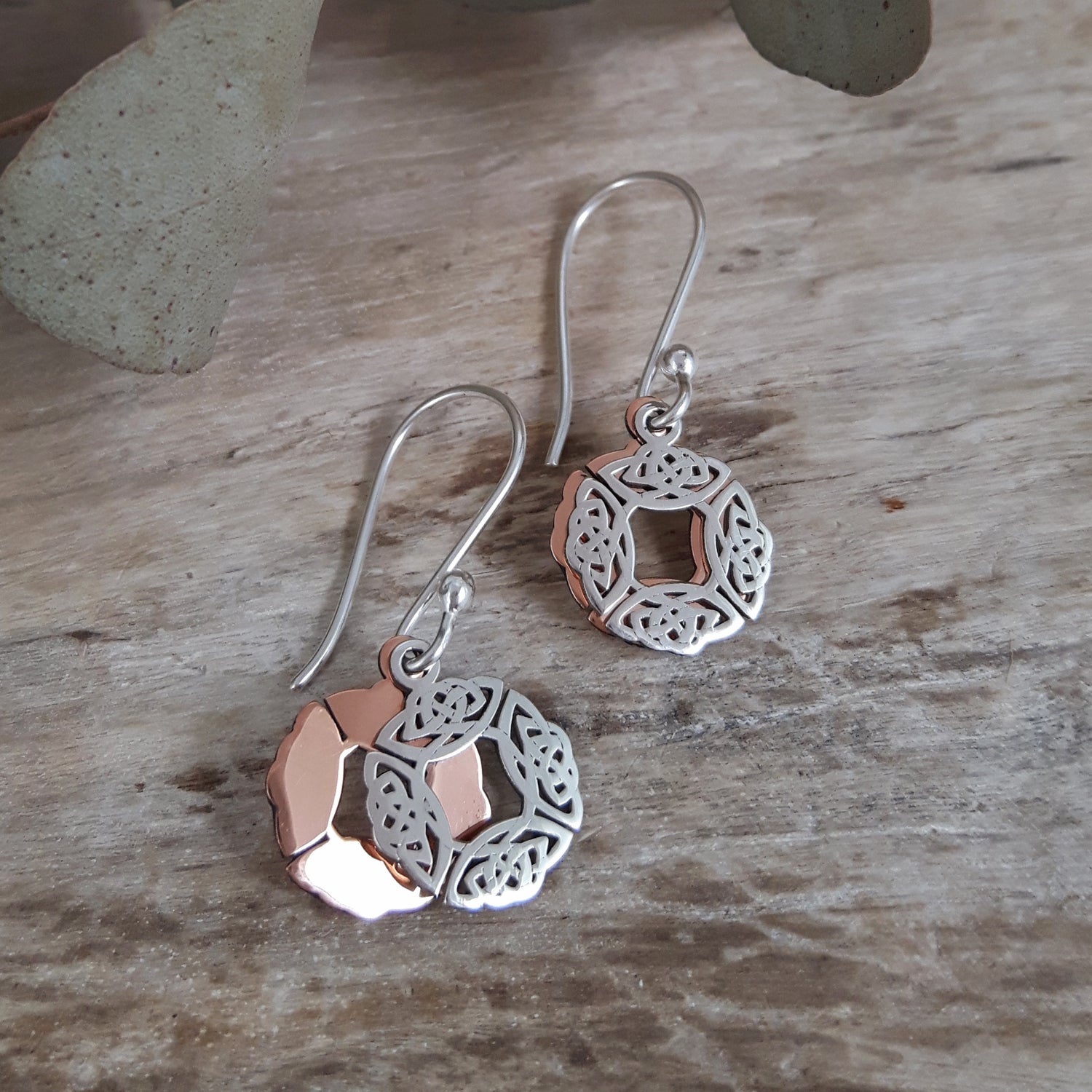 Pair of sterling silver and copper drop earrings on a wooden surface