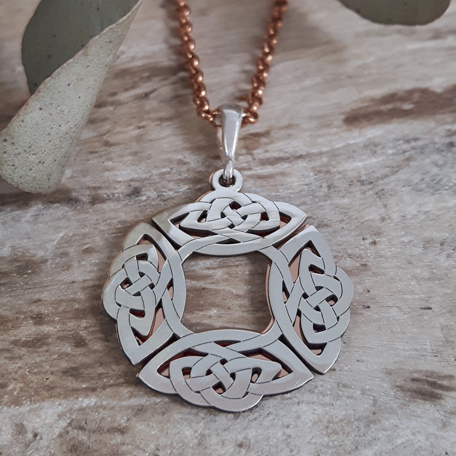Sterling silver & copper Celtic knot pendant on a wooden surface