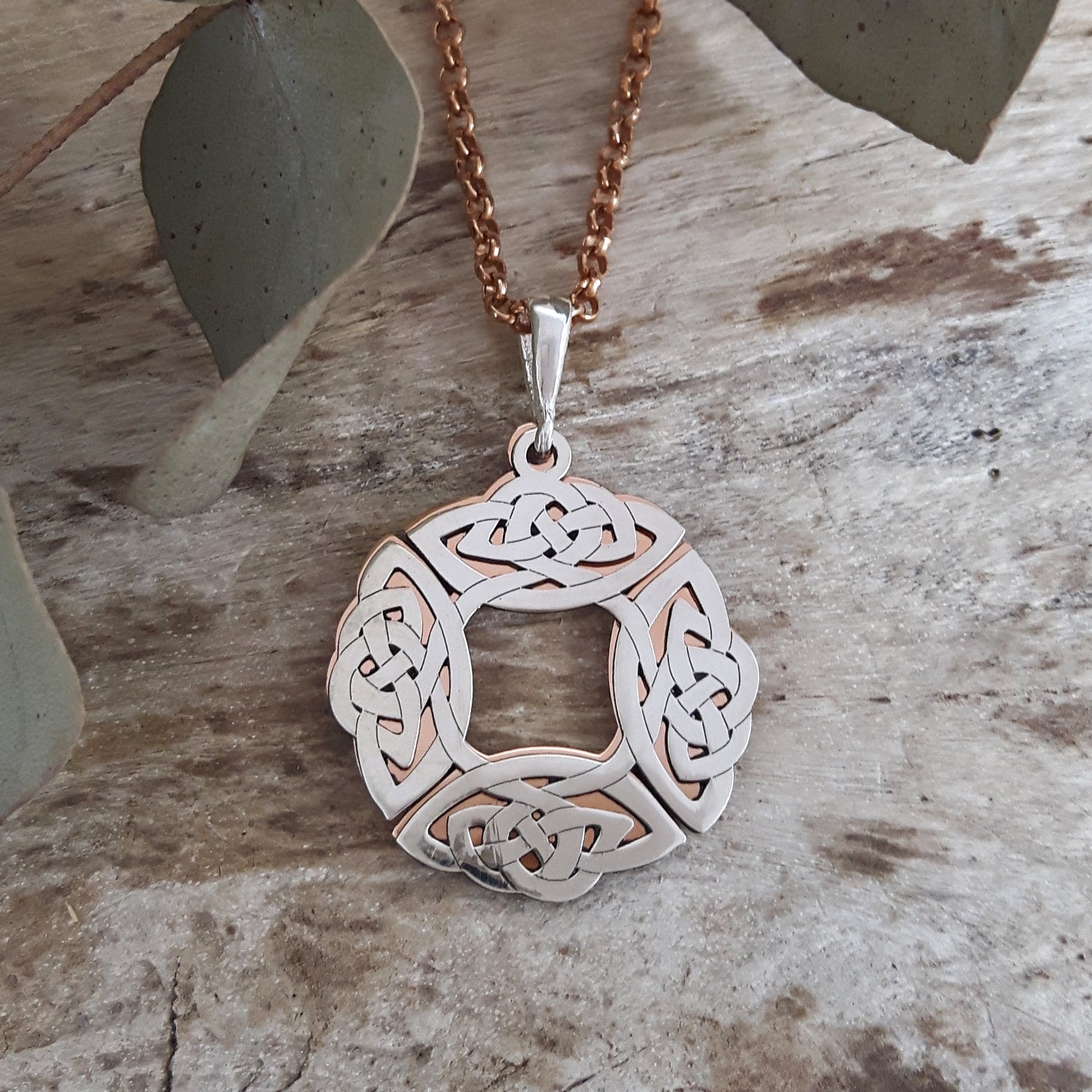 Sterling silver and copper Celtic knot pendant on a rose gold chain against a natural wood background
