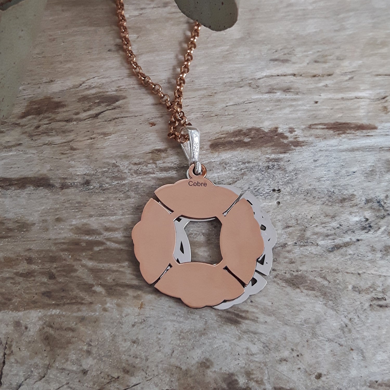 Back of a sterling silver and copper pendant on a wooden surface