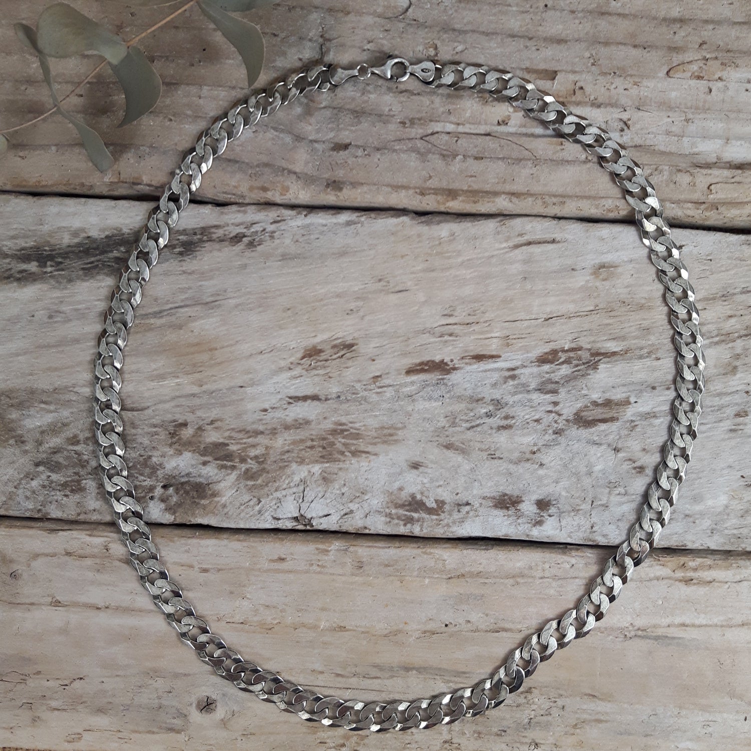 Sterling silver oxidised chain necklace on a wooden surface with a leafy branch.