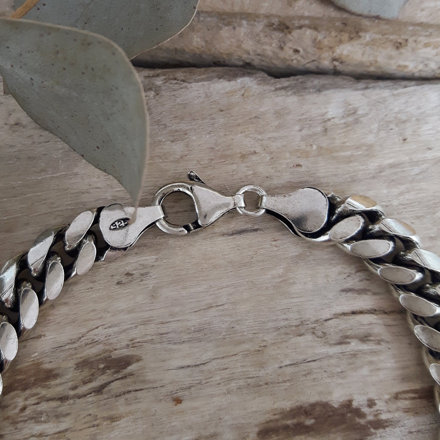 Mens sterling silver chain bracelet on a wooden surface with a leaf