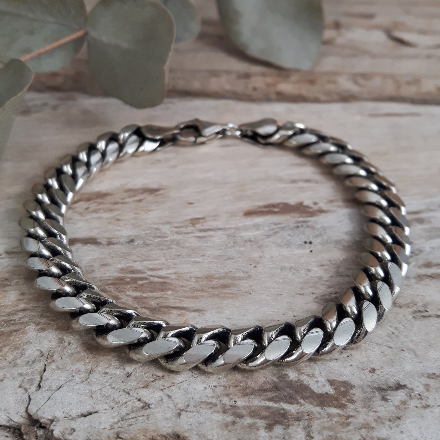 Sterling silver chain bracelet for him on a wooden surface with leaves in the background