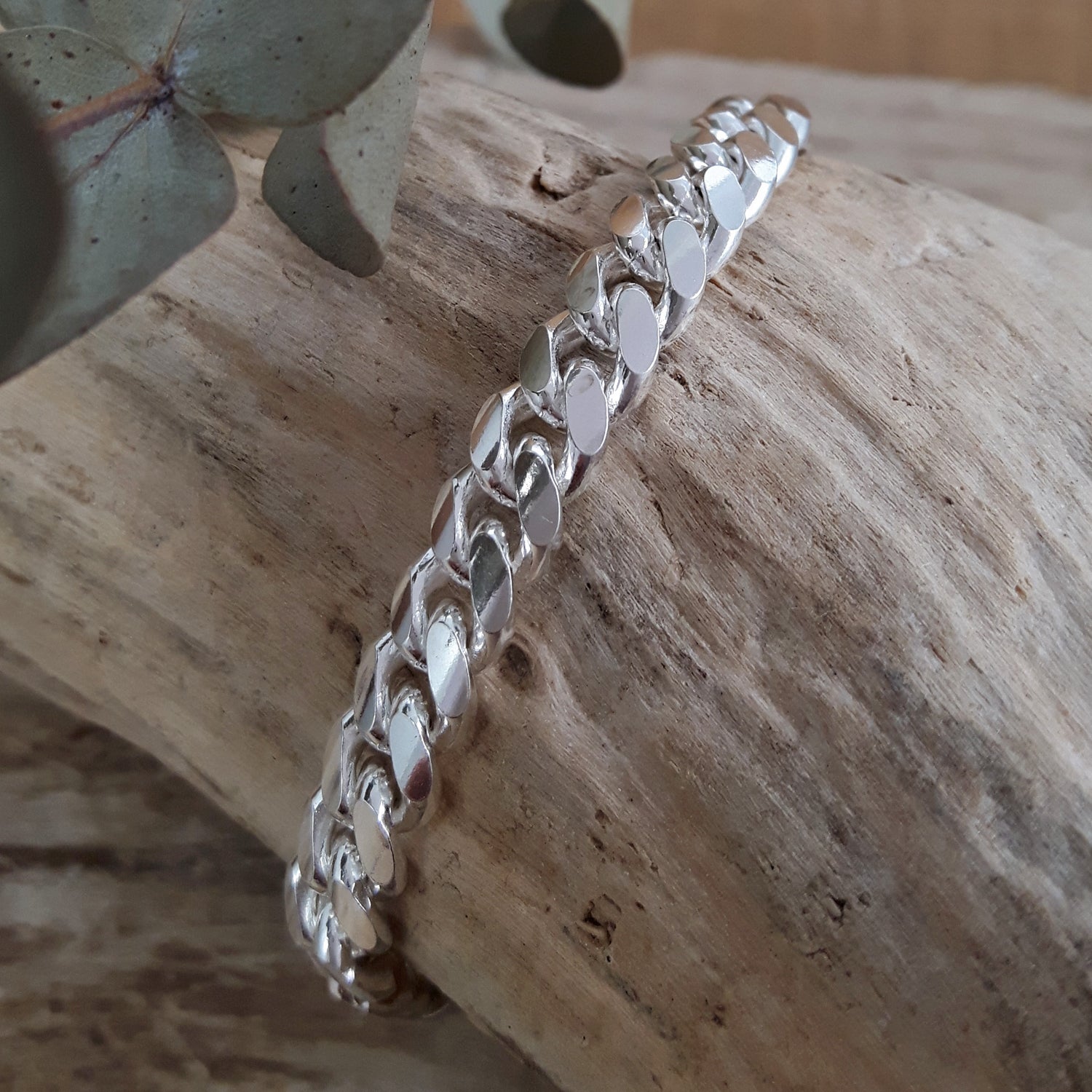Polished sterling siilver chain bracelet on a wooden surface with a leafy branch