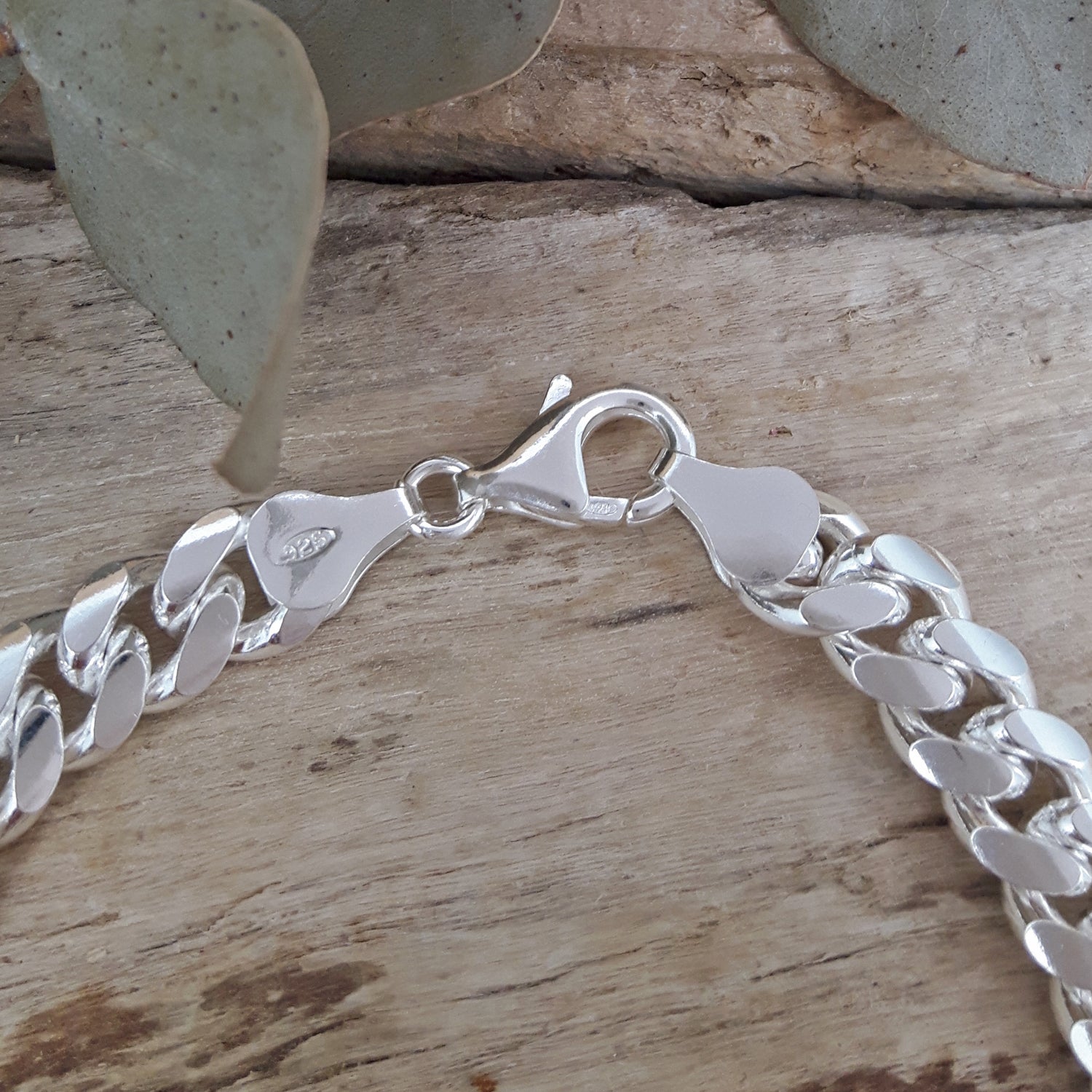 Polished sterling silver bracelet on a wooden surface with leaves in the background