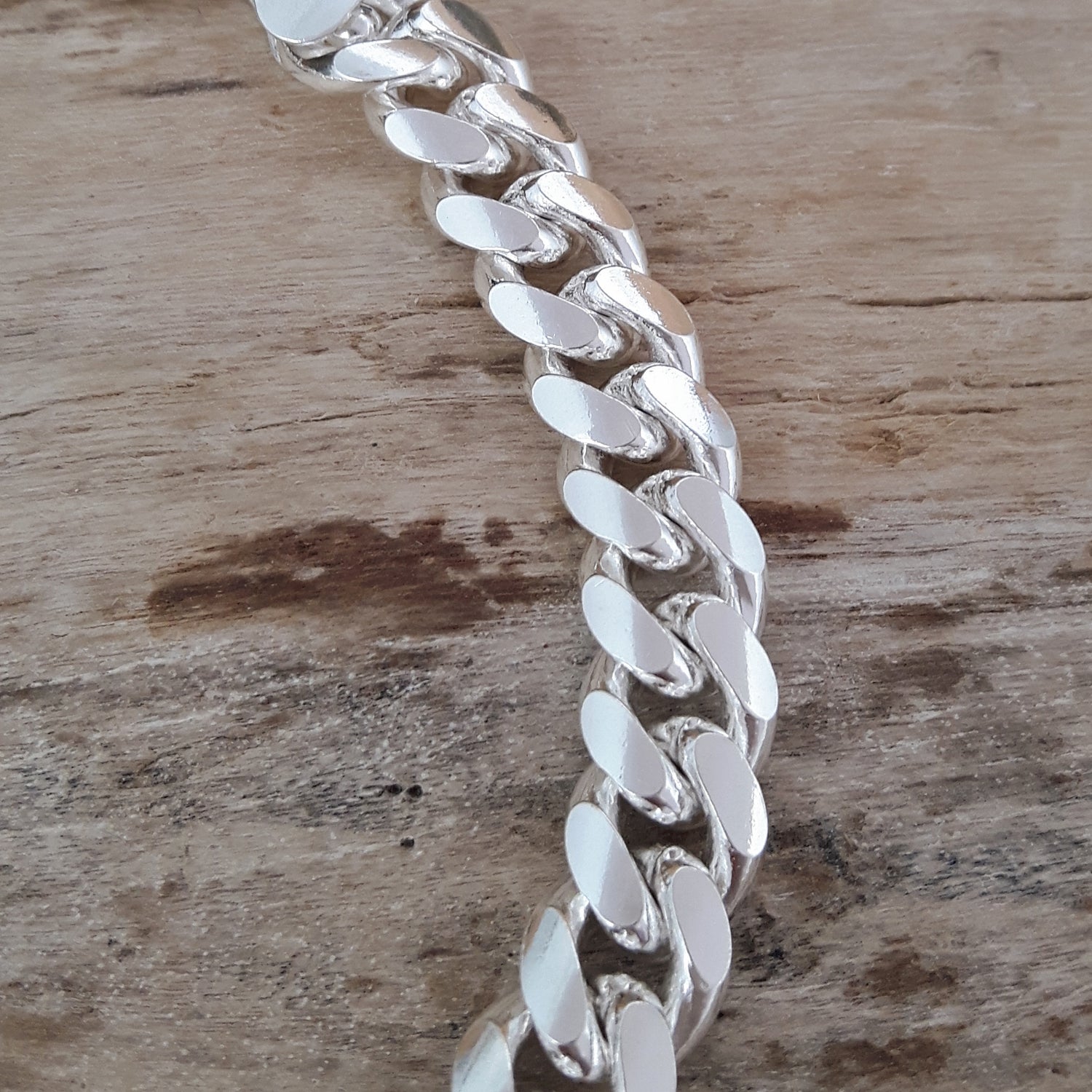 Polished unisex sterling silver chain bracelet on a wooden surface