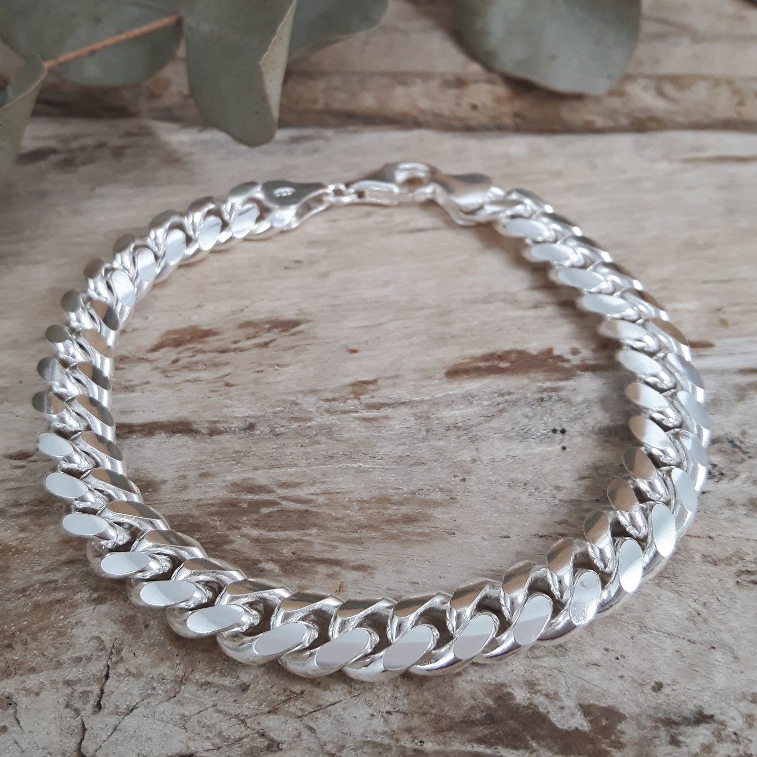 Polished sterling silver chain bracelet on a wooden surface with leaves in the background