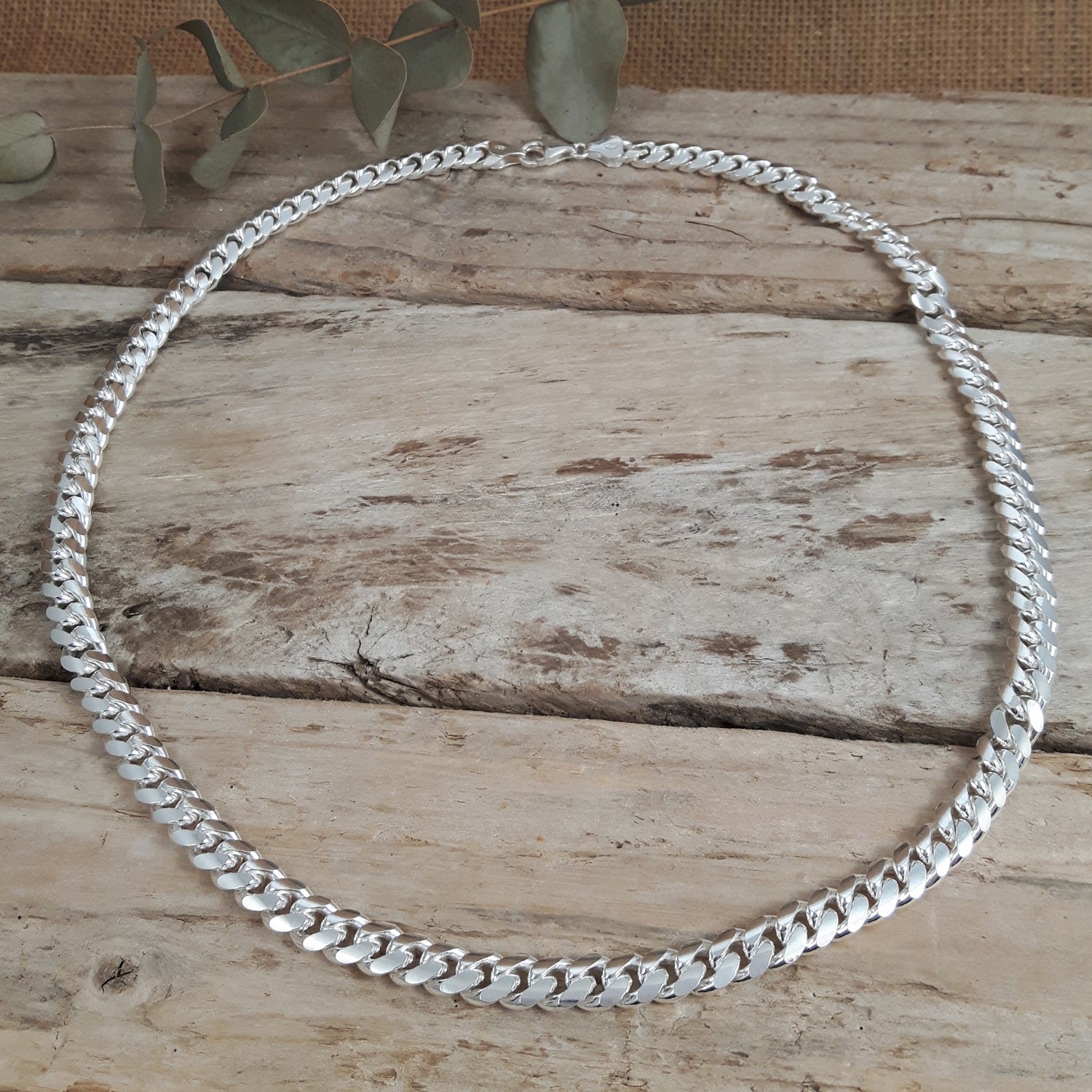 Mens sterling silver chain necklace on a wooden surface with green leaves in the background