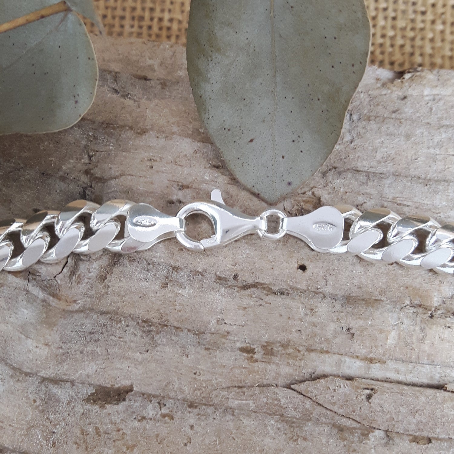 Polished sterling silver necklace on a textured surface with leaves in the background