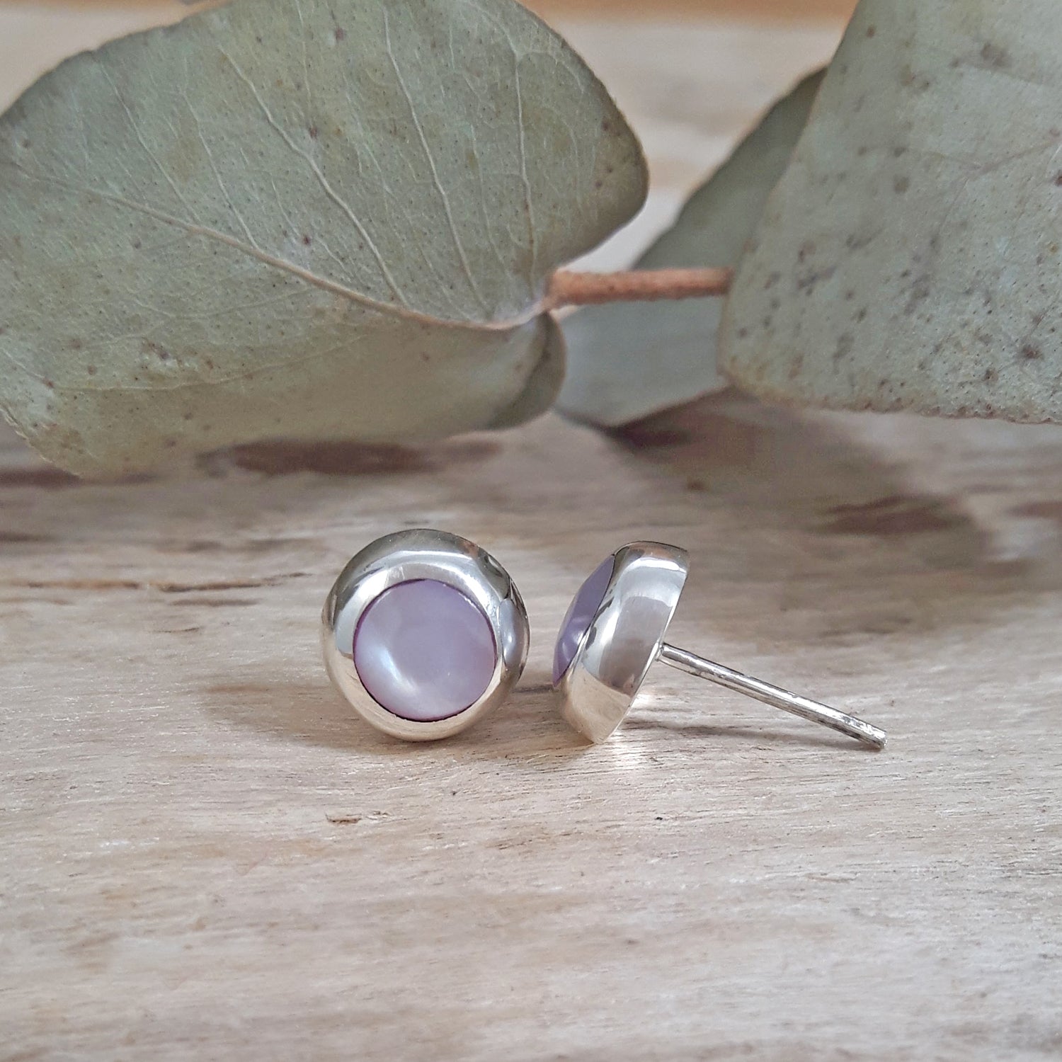 A pair of silver stud earrings with round side profile of 925 sterling silver pink mother of pearl circle stud earring showing stud post, soft pink shell