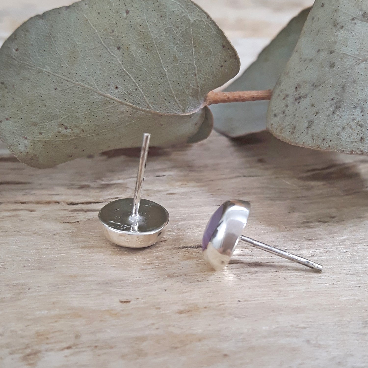 Back of 925 sterling silver pink mother of pearl circle stud earrings showing hallmark stamp and stud posts on driftwood.