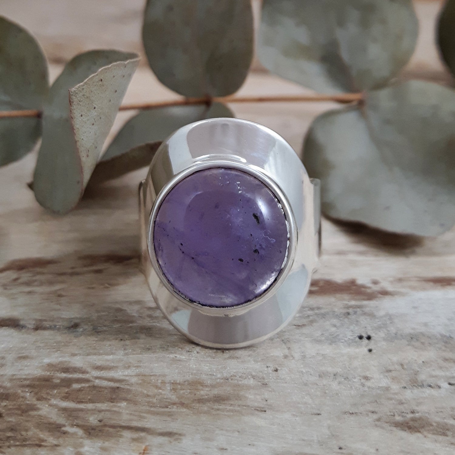 Unique sterling silver ring with a purple amethyst gemstone on a wooden surface with eucalyptus leaves.