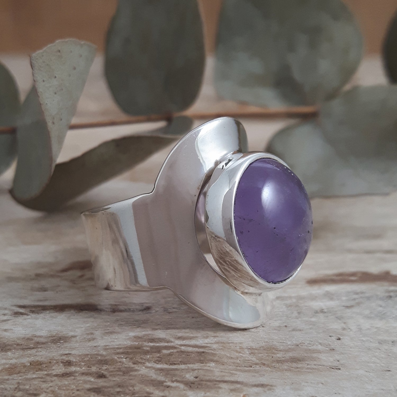 Sterling silver adjustable ring with a purple amethyst gemstone on a wooden surface with leaves in the background