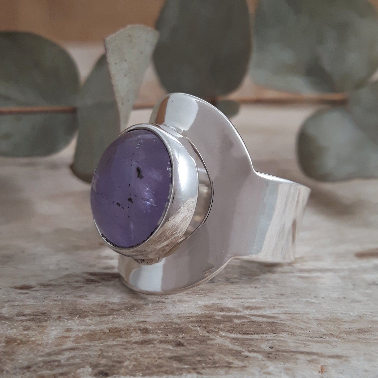 Sterling silver adjustable ring with a purple amethyst stone on a wooden surface with eucalyptus leaves in the background