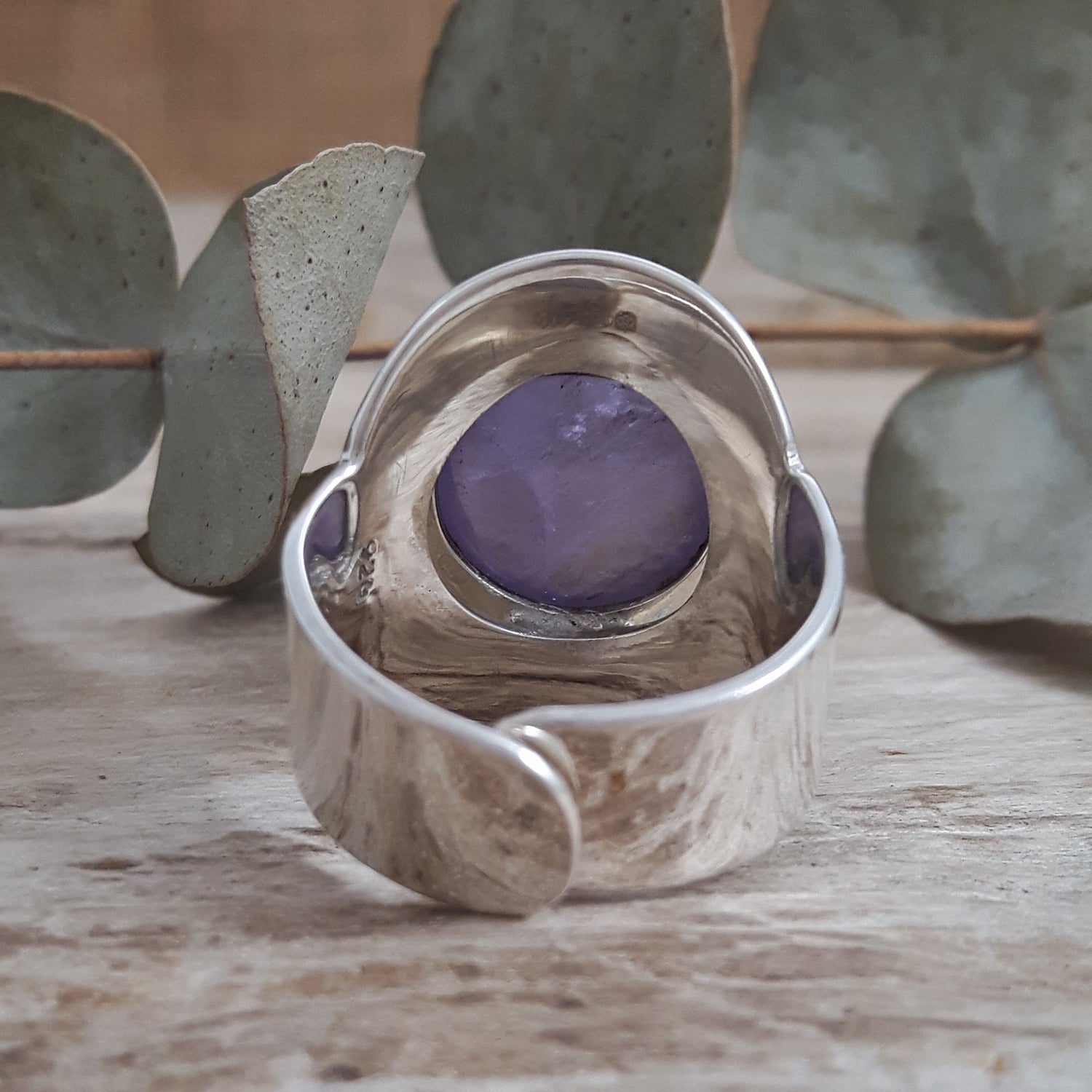 Unique sterling silver adjustable ring with a purple amethyst stone on a wooden surface with eucalyptus leaves.