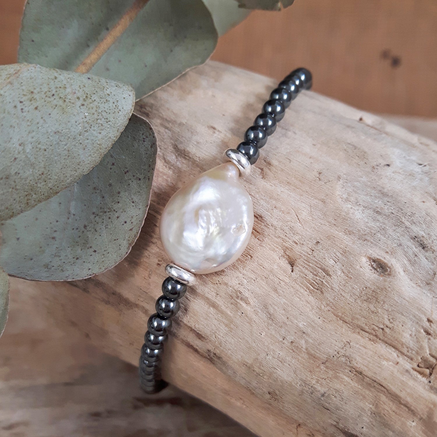 Hematite beaded bracelet with a large pearl on a wooden surface with leaves. Designed in the UK.