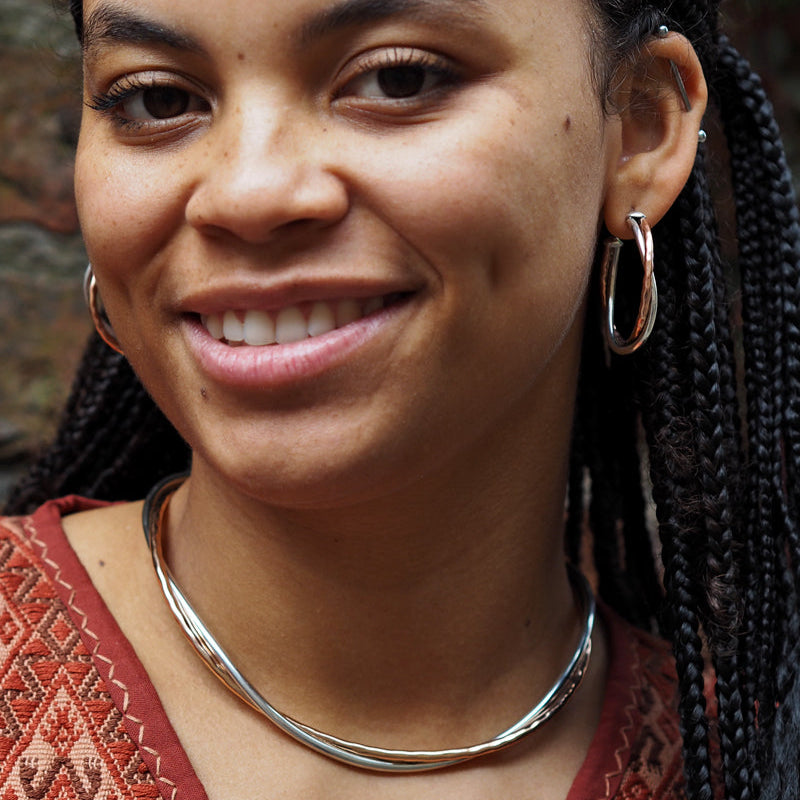 Woman with braided hair wearing a red patterned top and copper and silver necklace choker.