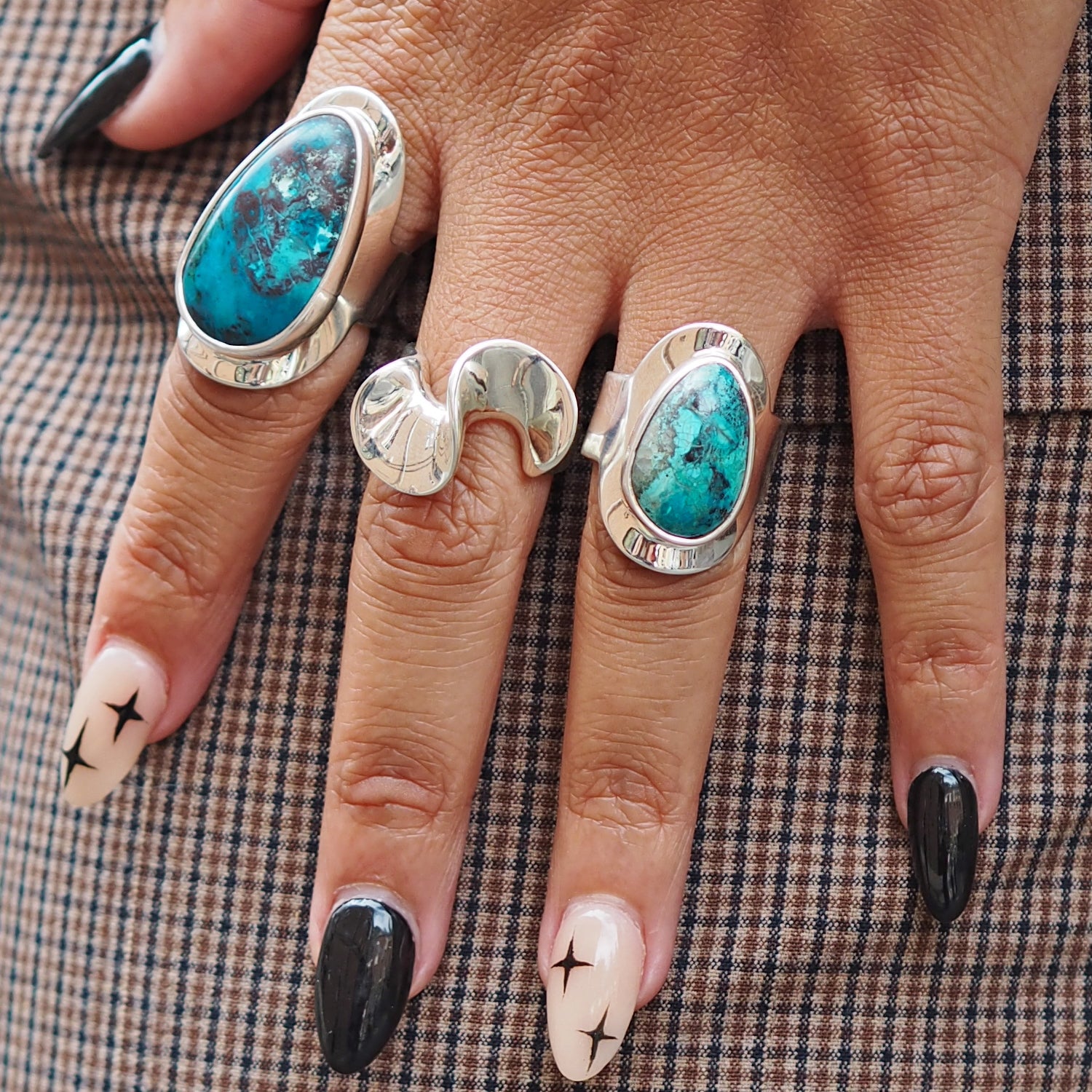 Hand wearing three sterling silver rings 2 with shuttakite stones on a checkered fabric background