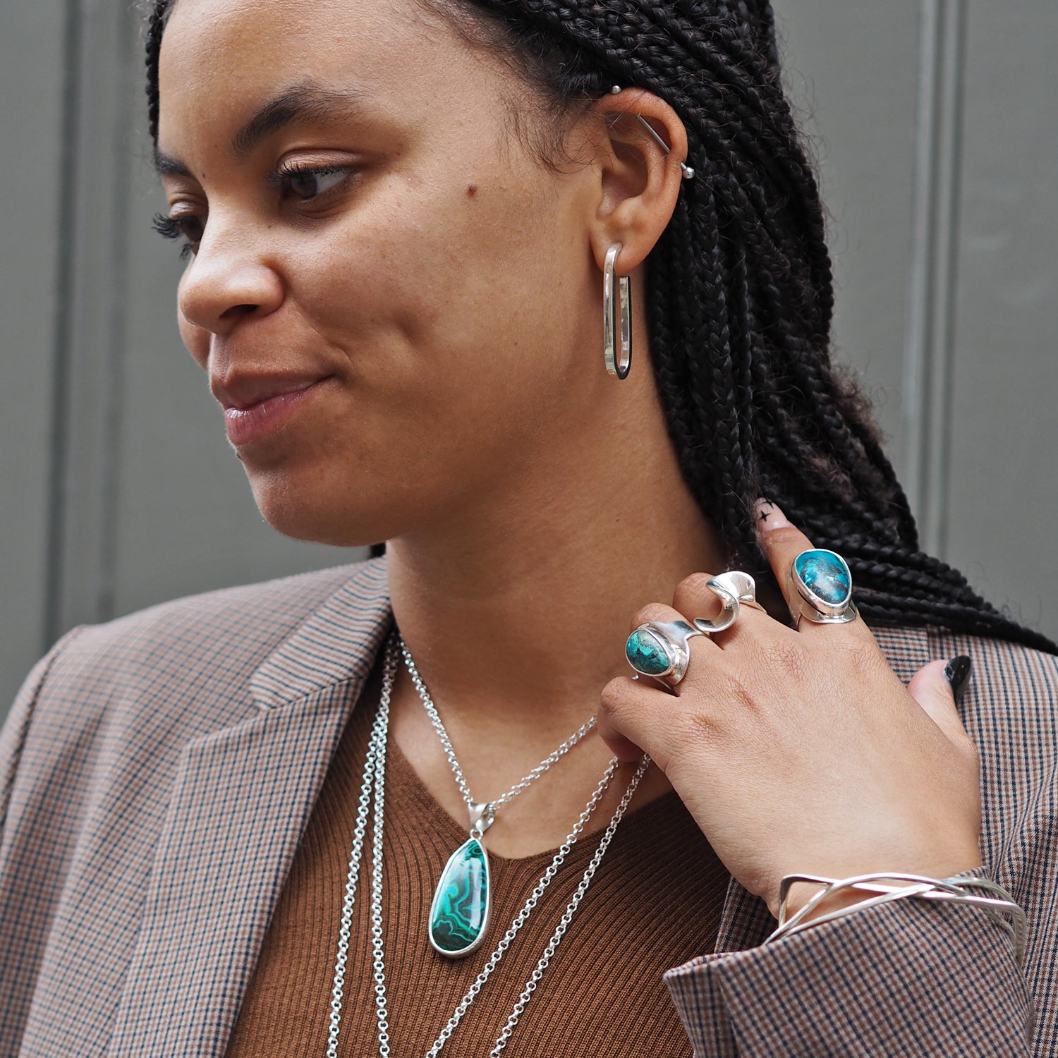 Woman wearing turquoise jewellery, including rings and a pendant on a chain, with a neutral background