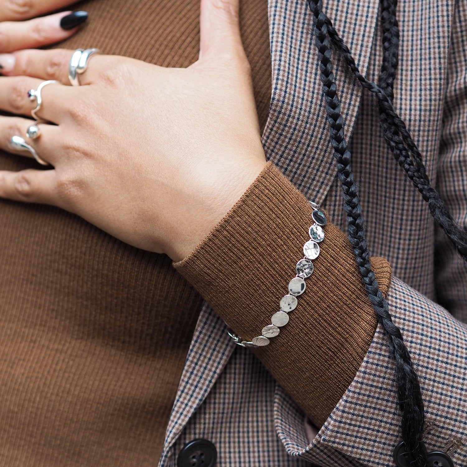 Close-up of a person wearing a silver bracelet with a brown sleeve and plaid shirt.