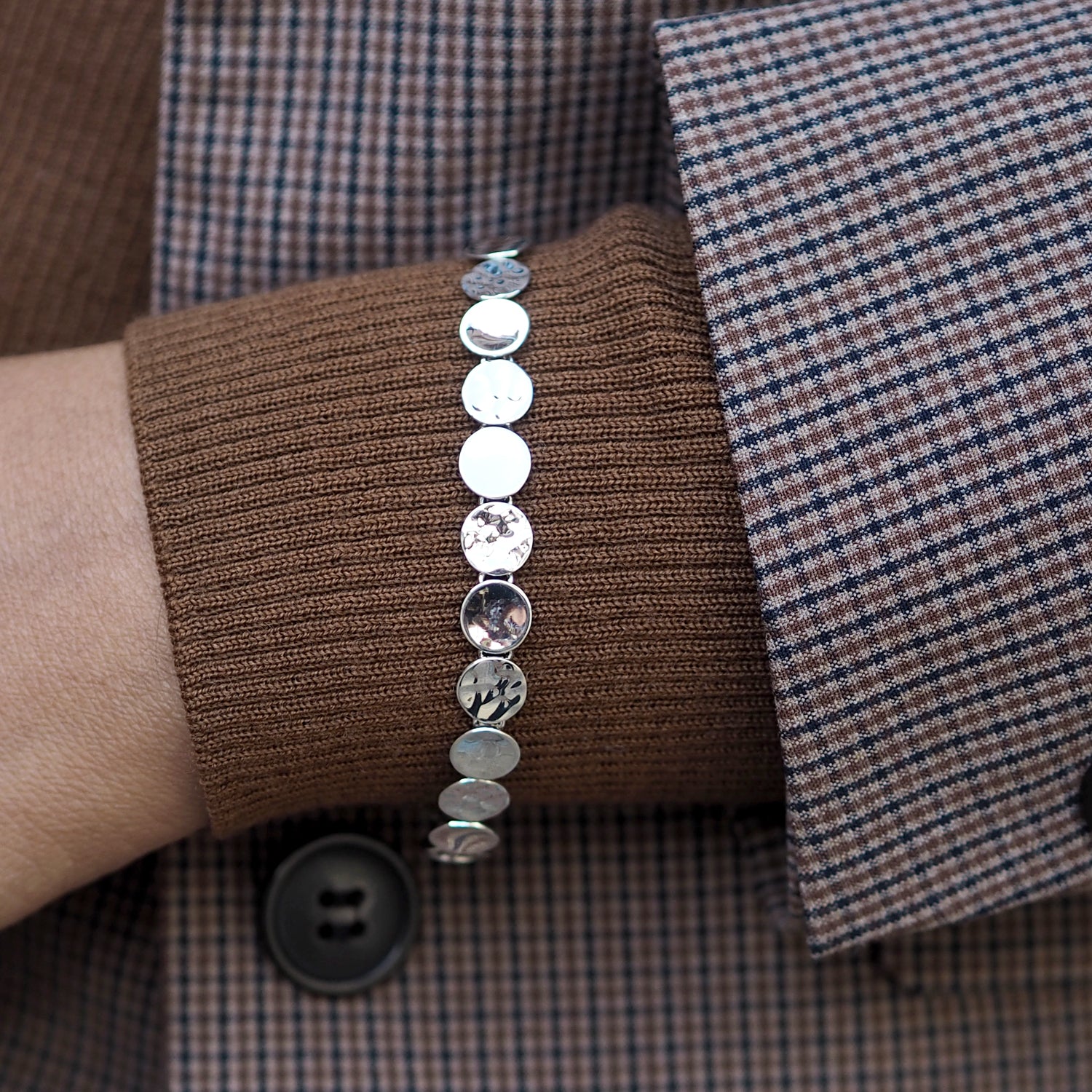 Silver bracelet on a wrist with a plaid shirt and brown fabric background