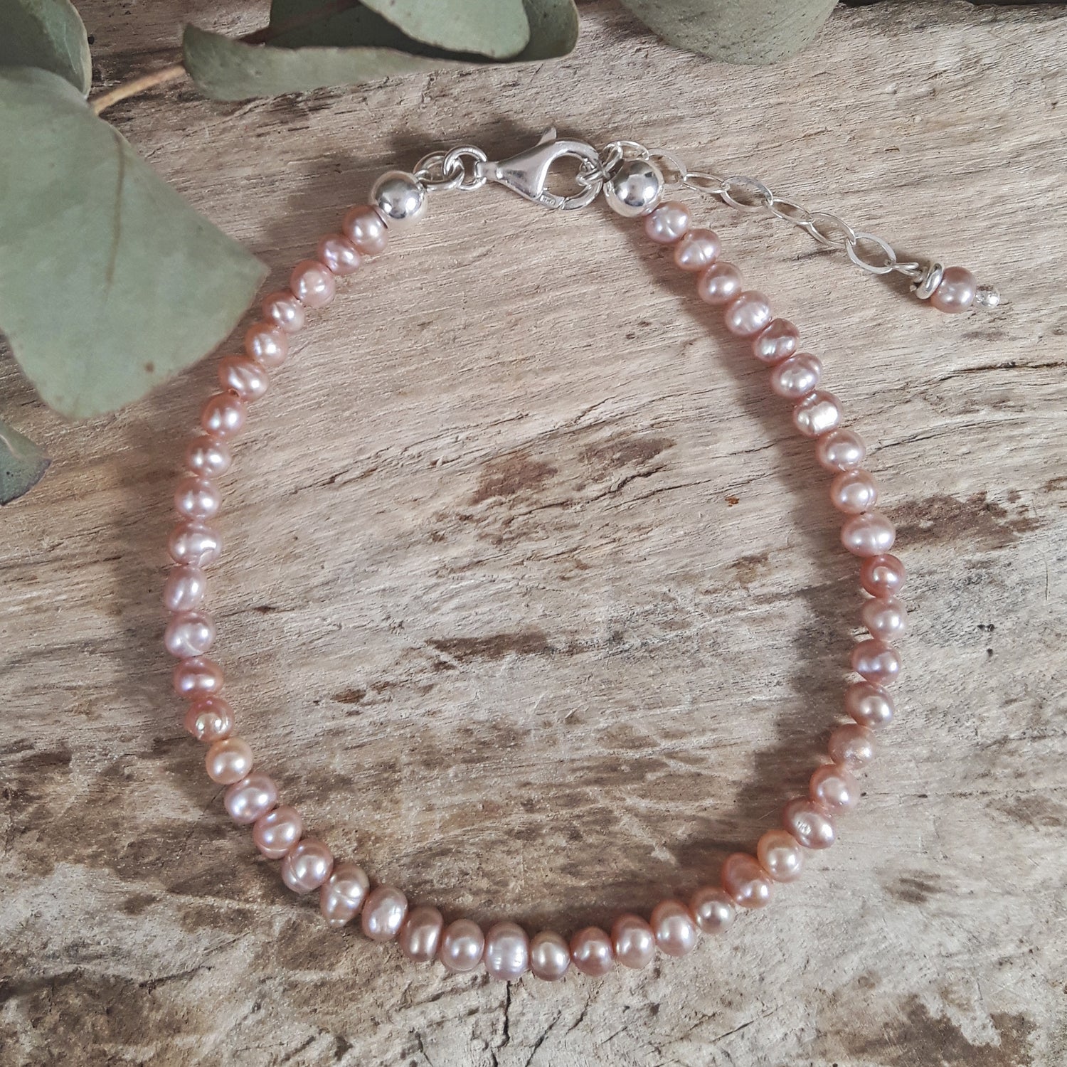 Pearl bracelet on a wooden surface with green leaves