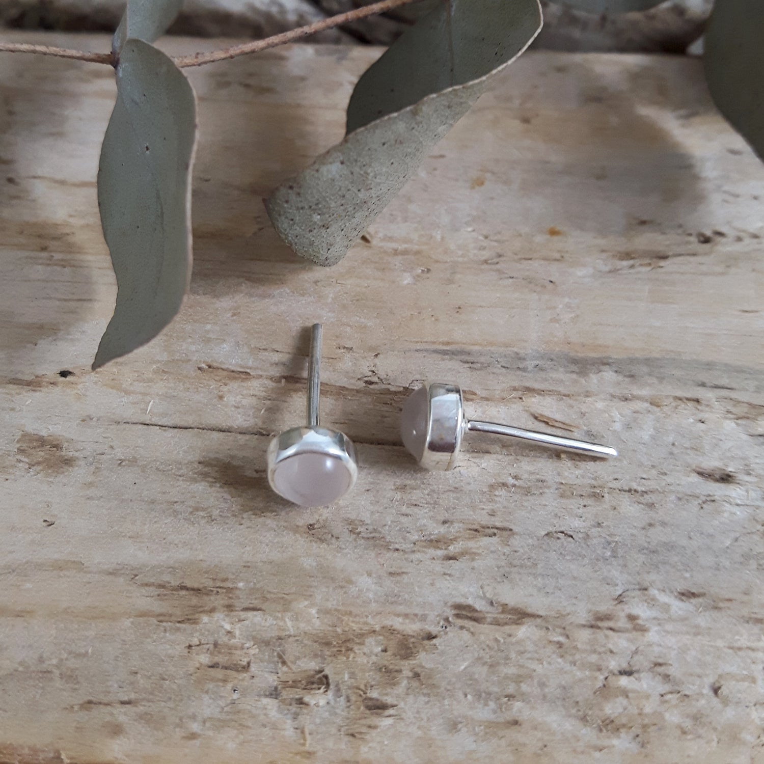 Rose Quartz sterling silver stud earrings on a wooden surface with eucalyptus leaves