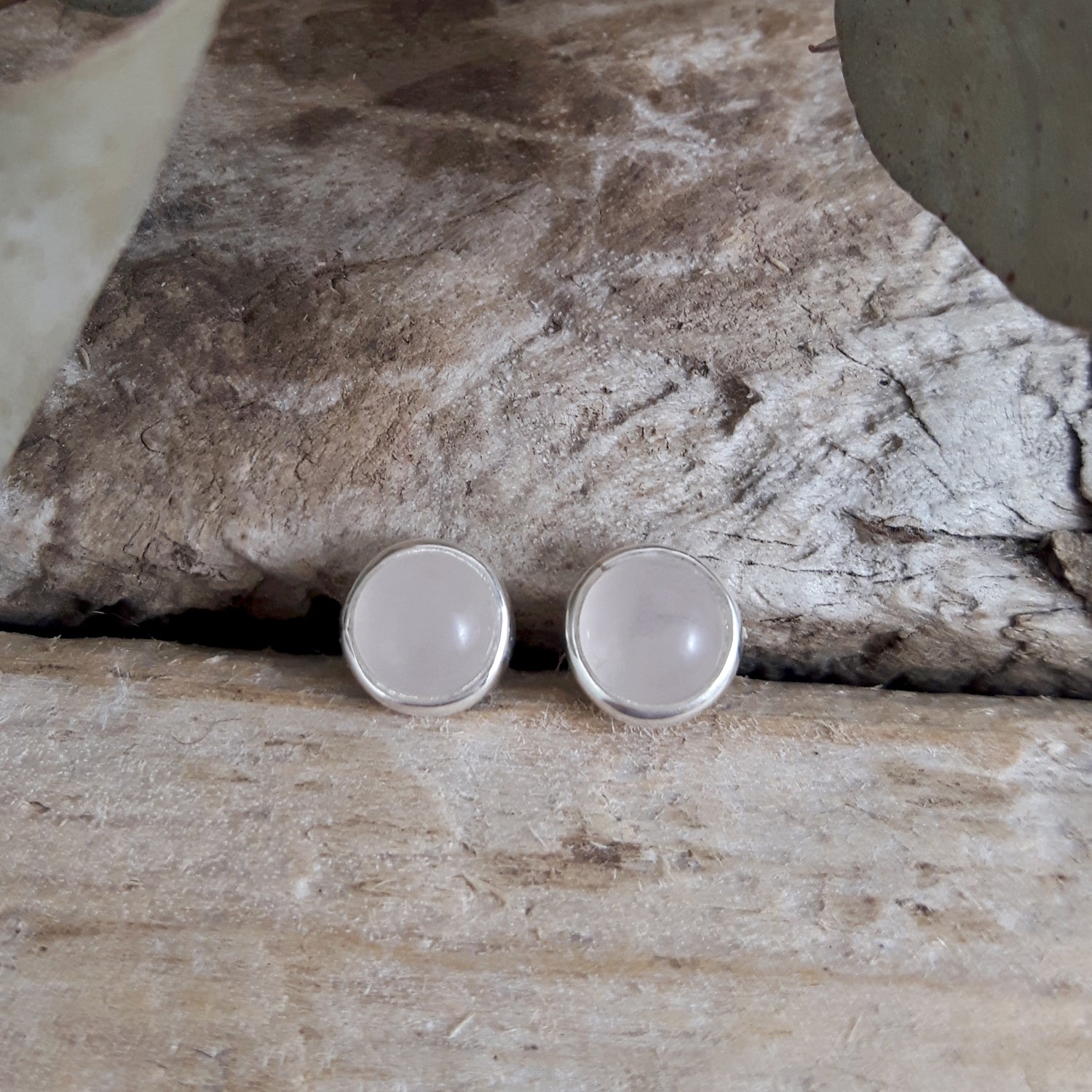 Round sterling silver stud earrings with rose quartz centre on a wooden backdrop