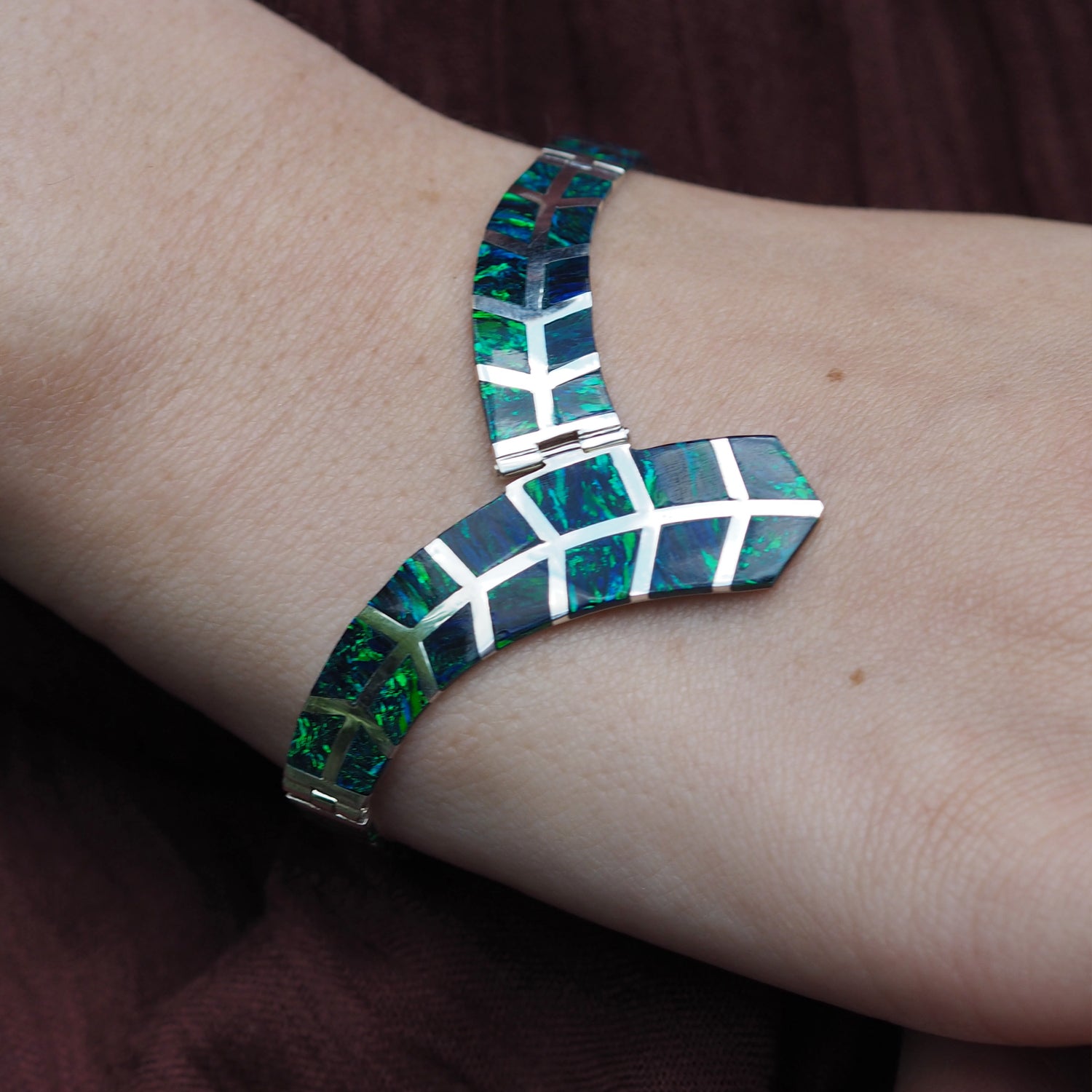 Sterling silver bracelet with emerald cultured opal detail worn on a wrist against a dark background