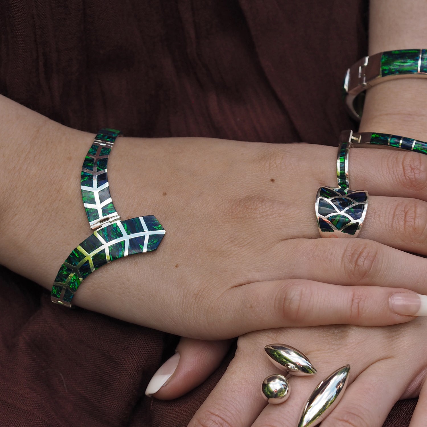 Close-up of a hand wearing an emerald cultured opal and sterling silver bracelet and ring on a brown background